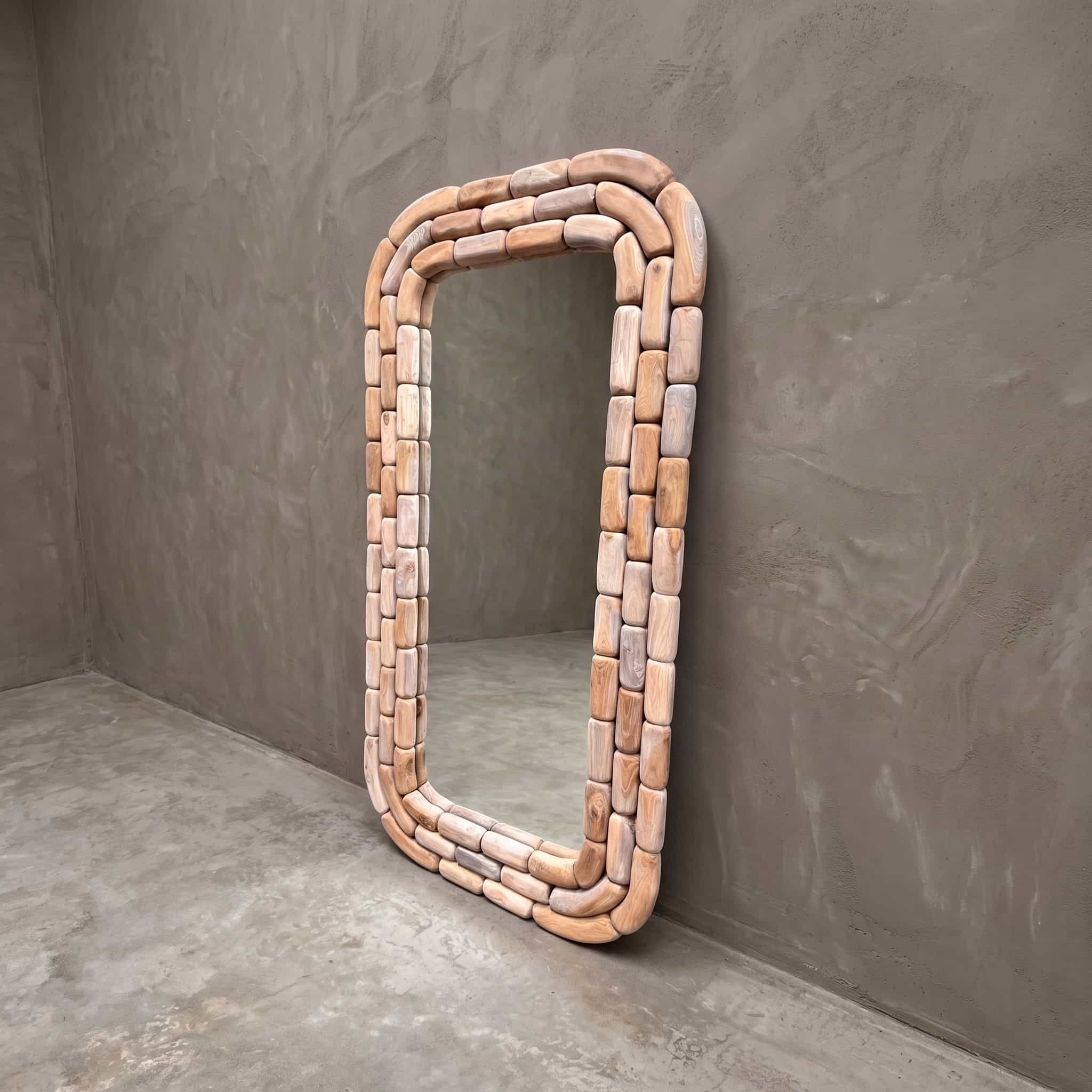 Spiegel Arunja van gerecycled teak, 180 cm hoog, schuin van voren gezien, met een lijst van afgeronde blokjes tegen een grijze wand