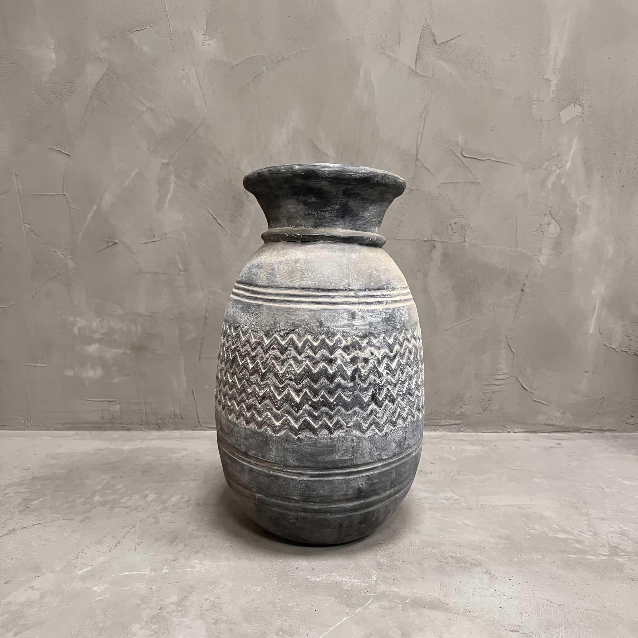 Pot Dongdong van polystone, vooraanzicht van de bolle pot met zigzagband en smalle hals tegen een grijze wand