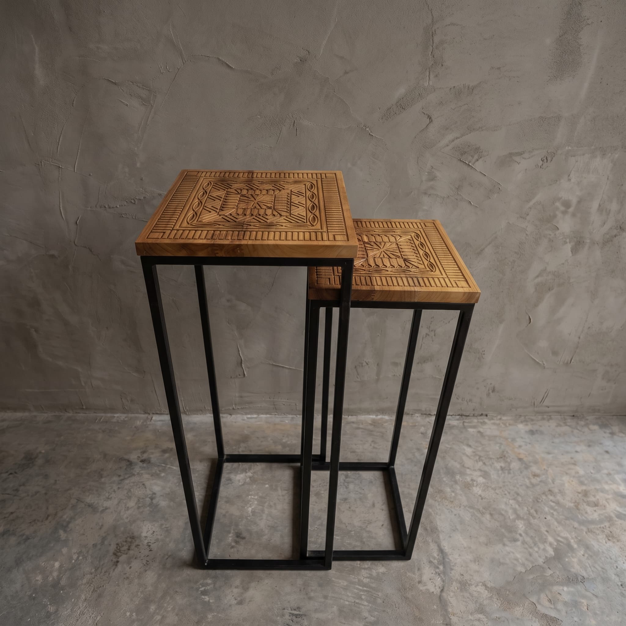 Intan teak display, set of 2, seen from above at an angle: two square tops with a geometric pattern on black frames
