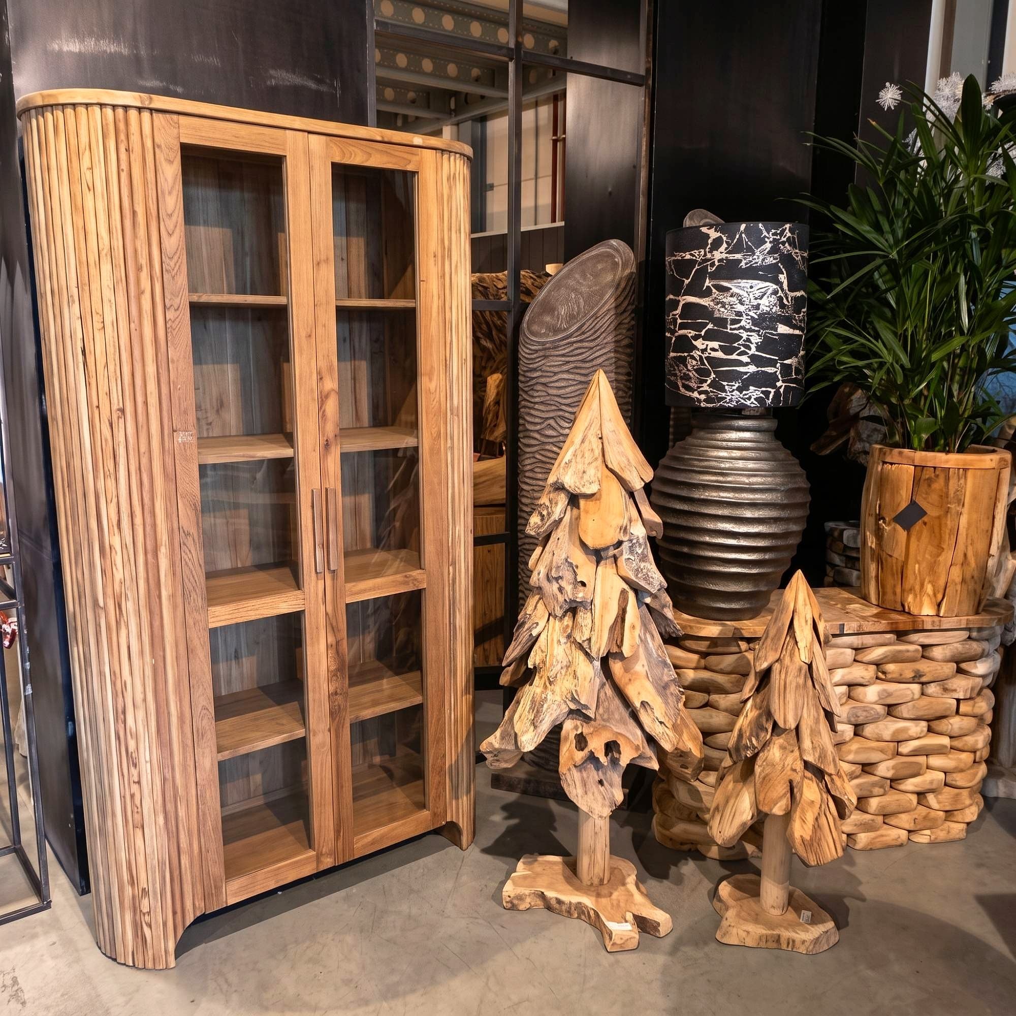 Kast Rujen van gerecycled teak, met glas, schuin vooraanzicht in de showroom naast twee houten kerstbomen en een lamp