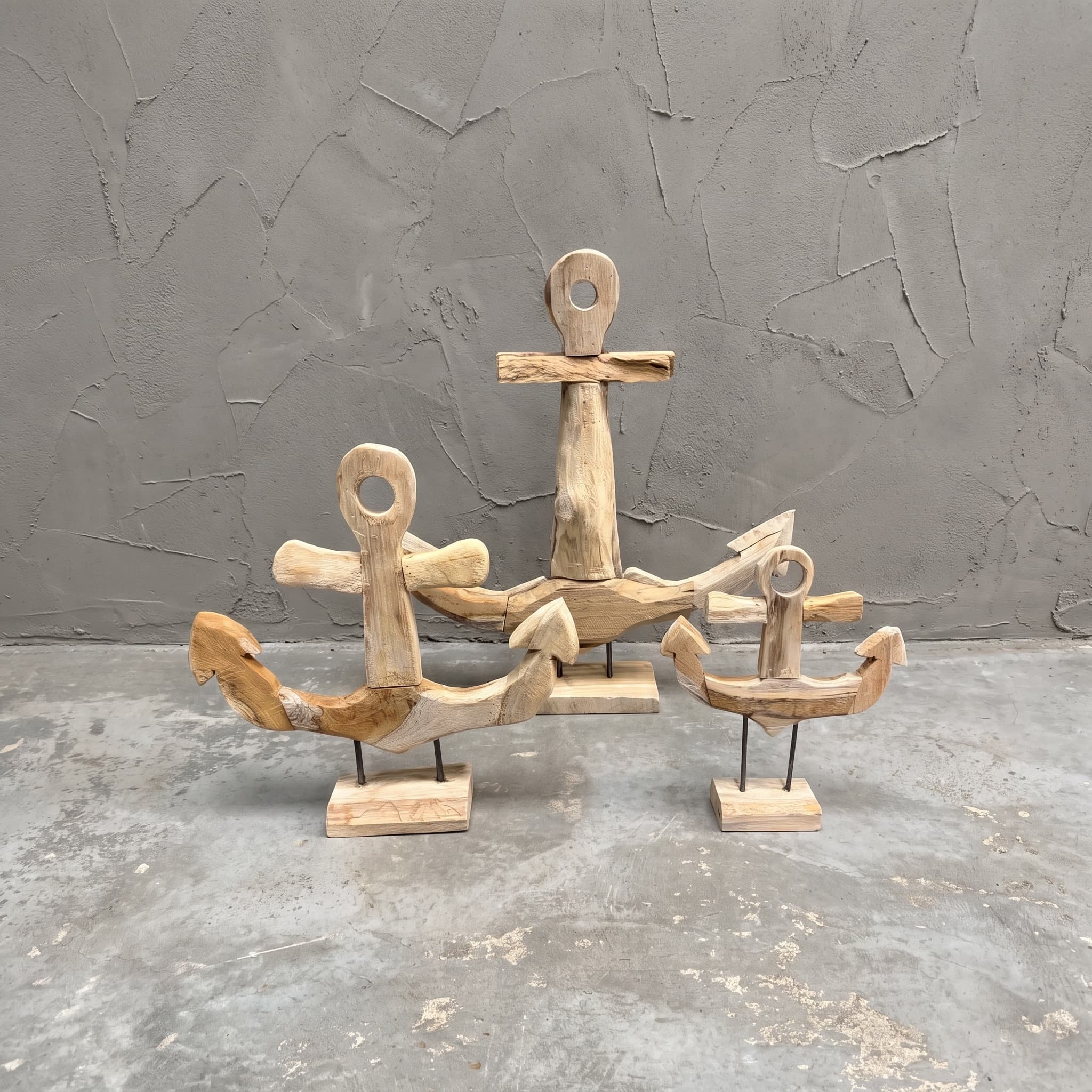 Sockel aus recyceltem Teak, Anker, 3er-Set, Vorderansicht der drei Anker auf ihren Füßen vor grauer Wand