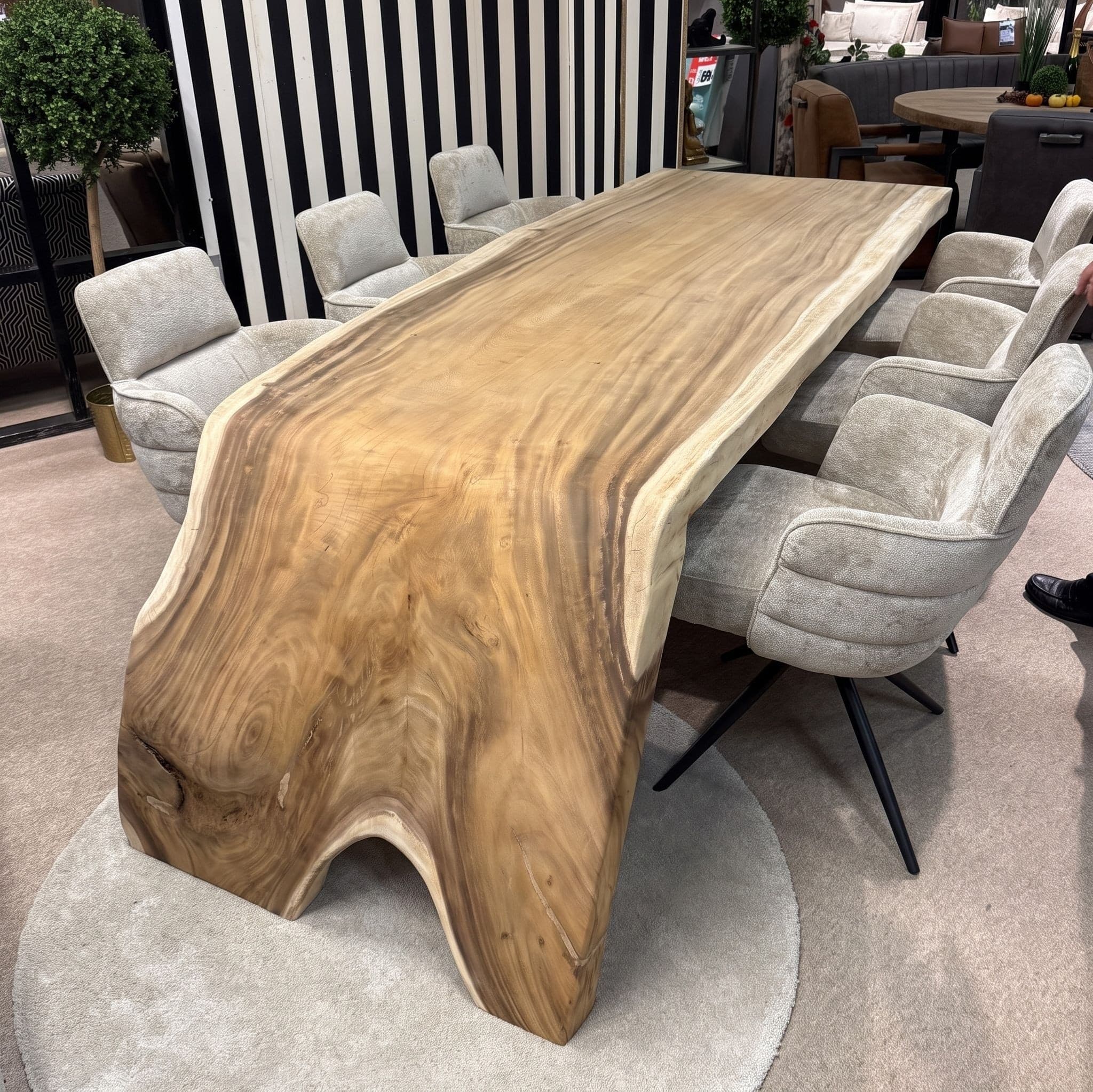 Eettafel van suarhout, rivier, in een winkel met beige stoelen, het omgebogen tafeleind op een rond vloerkleed