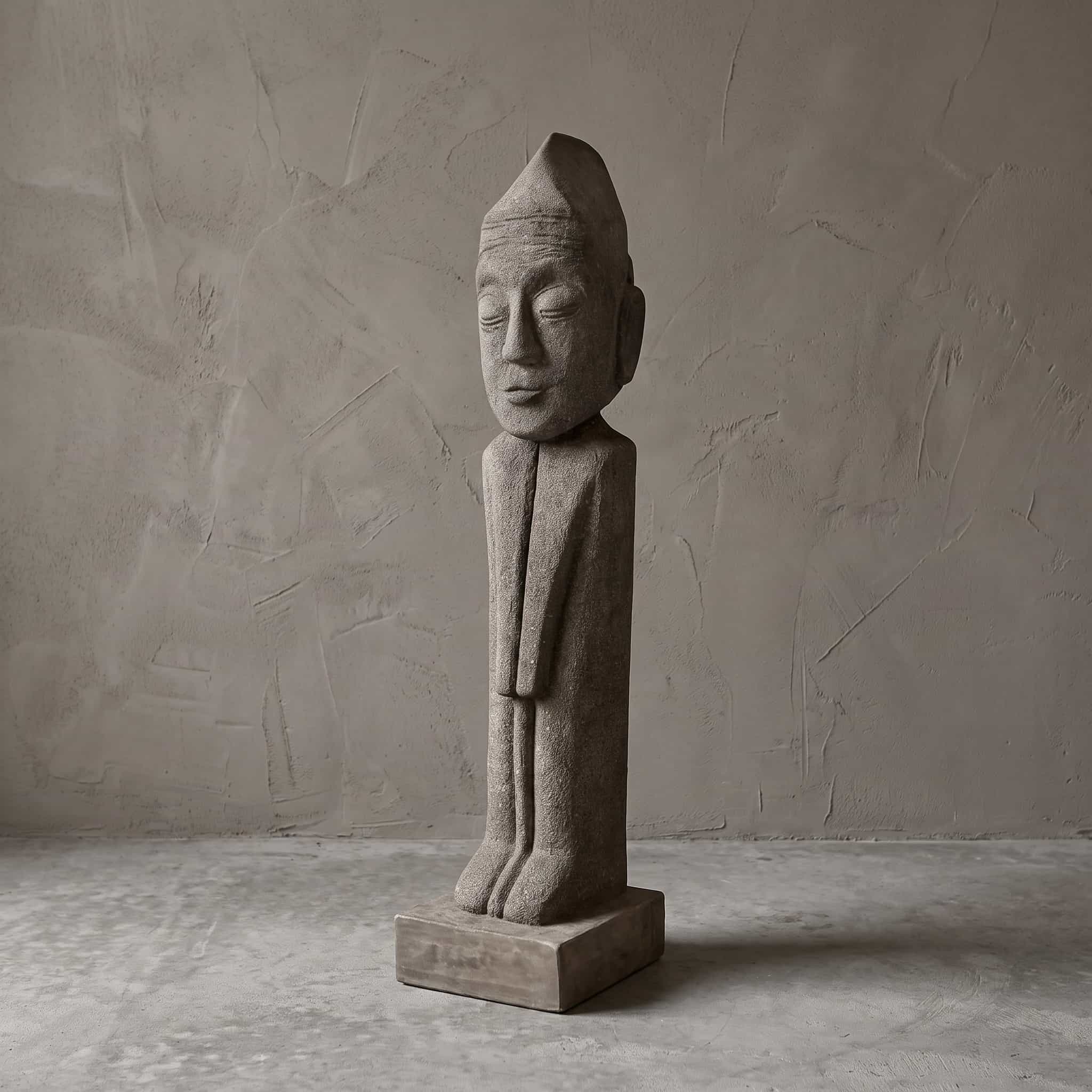 Beeld Konggo 1 van polystone, slanke grijze figuur met puntmuts, gesloten ogen en een lichte glimlach, staand op een vierkant blok