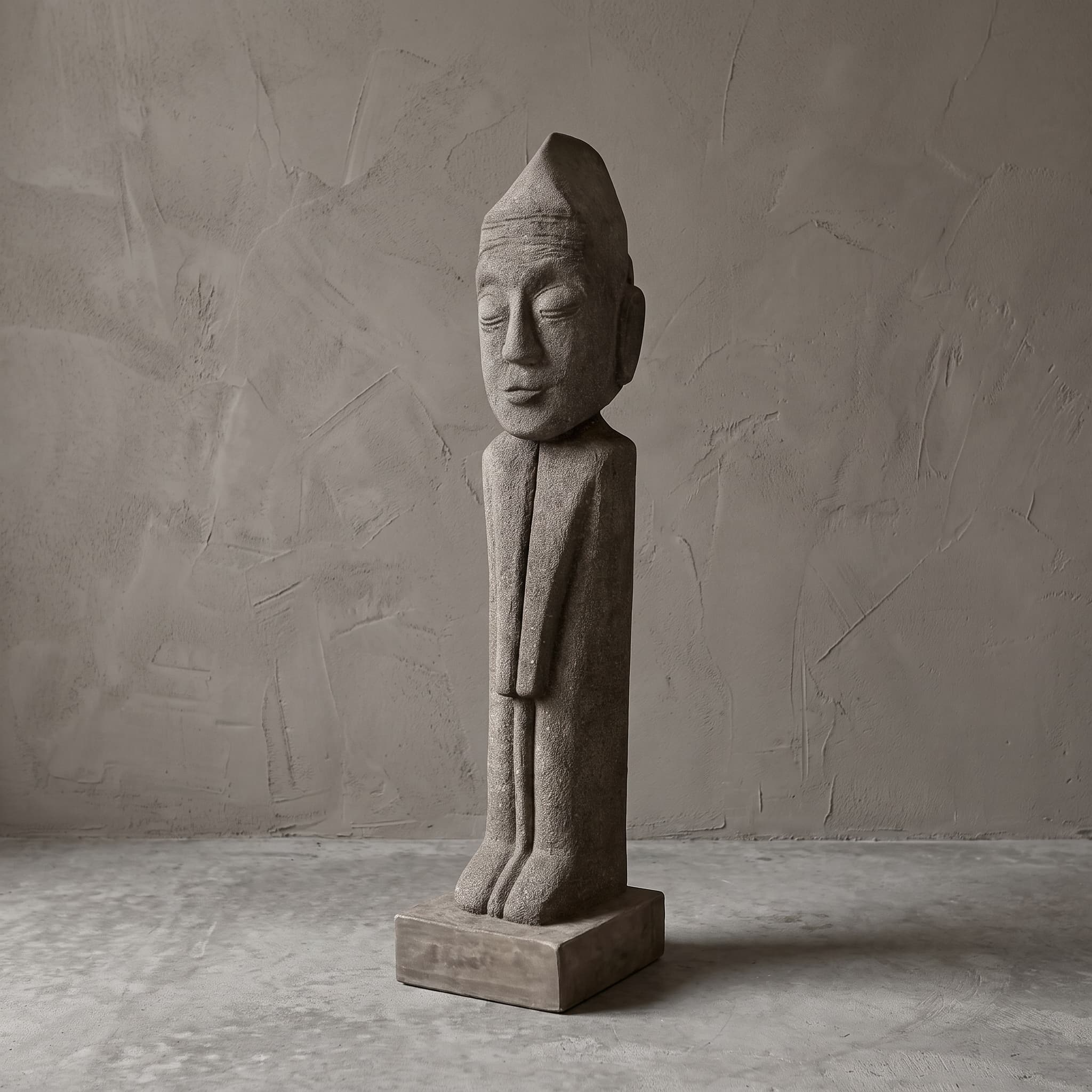 Beeld Konggo 1 van polystone, slanke grijze figuur met puntmuts, gesloten ogen en een lichte glimlach, staand op een vierkant blok