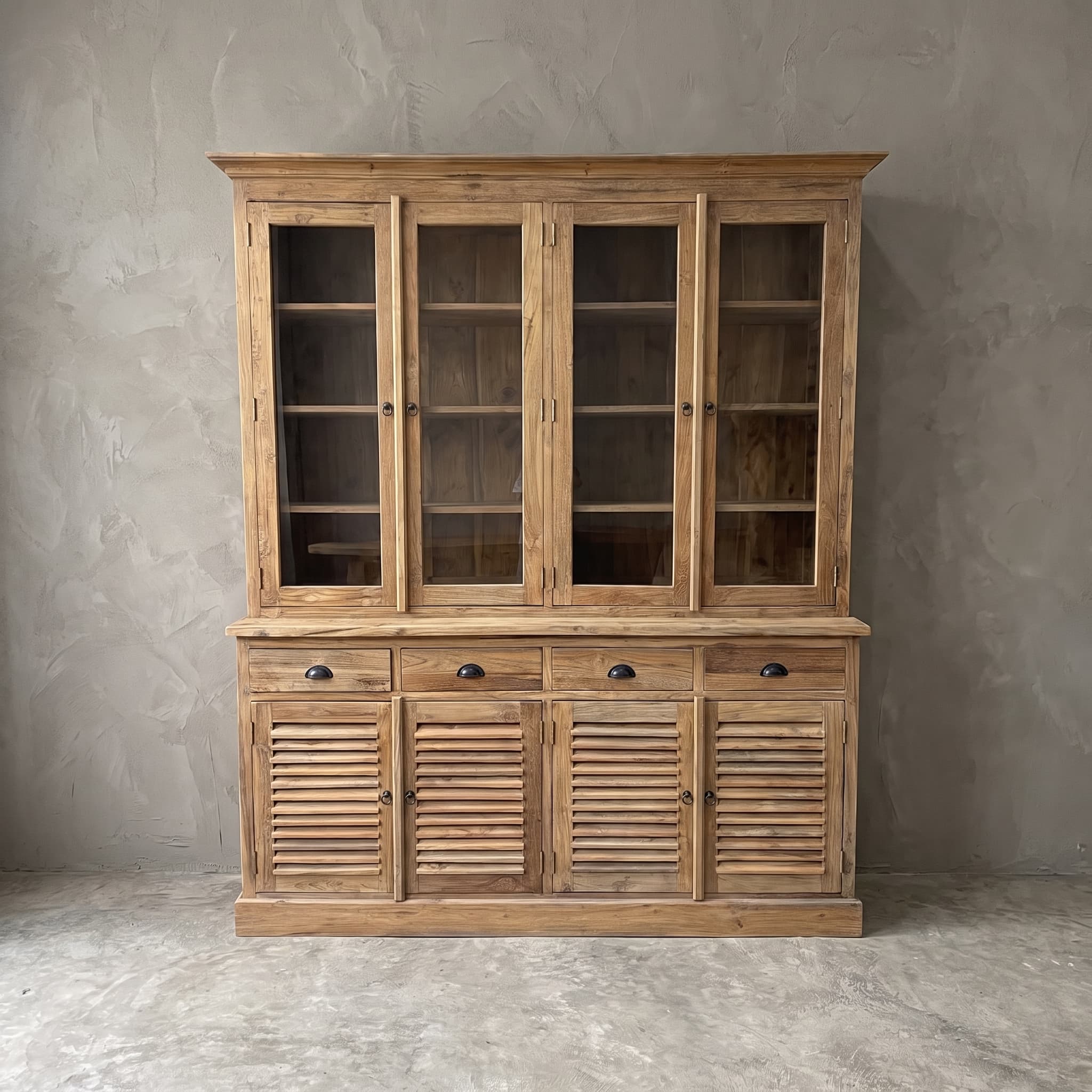 Kast Bali Tumpuk van gerecycled teak recht van voren tegen een grijze wand, glazen deuren voor de planken en donkere komgrepen op de lades
