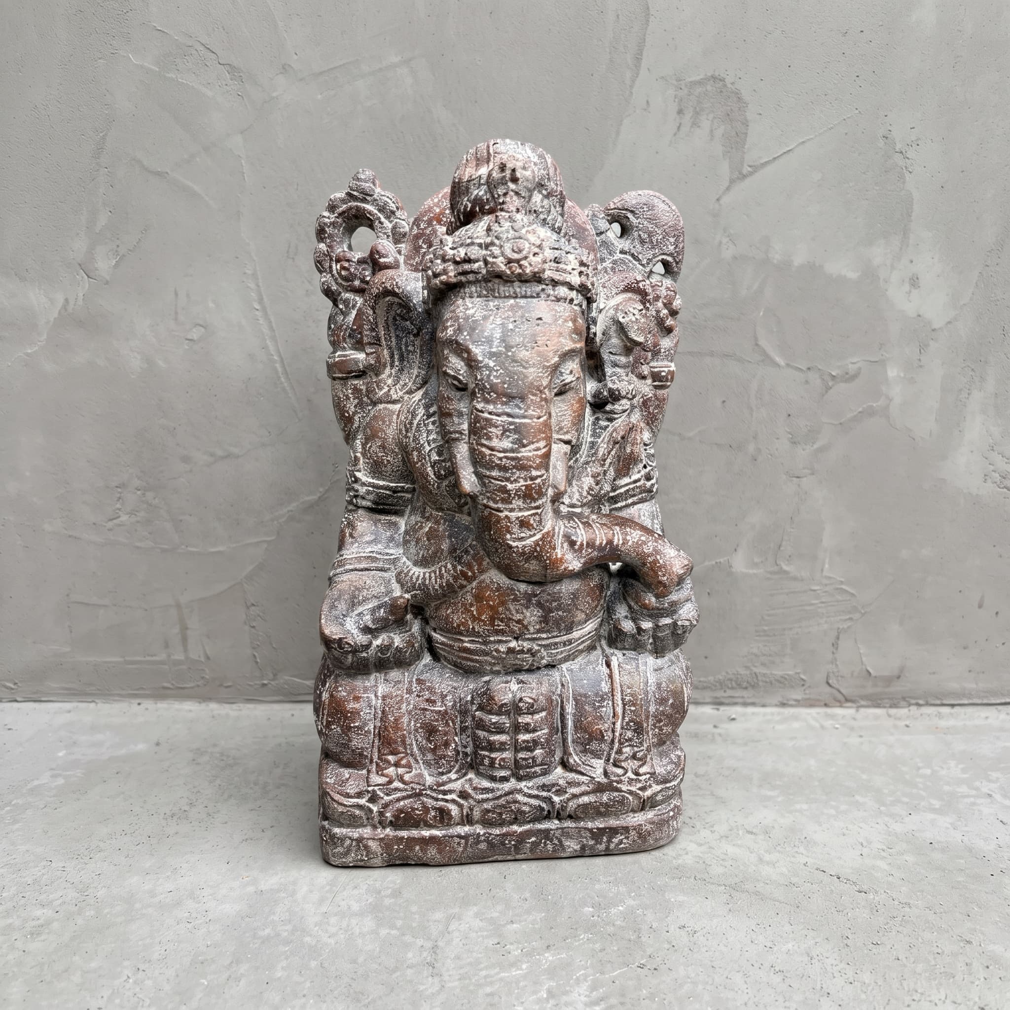Beeld Ganesha van polystone, vooraanzicht van de zittende Ganesha met kroon en gekrulde slurf voor een grijze wand
