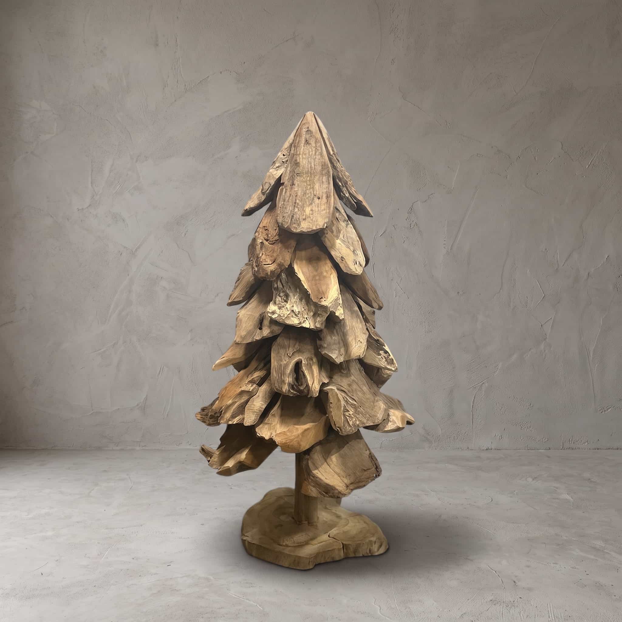 Kerstboom van gerecycled teak, vooraanzicht van de gelaagde stukken hout rond de stam op een platte voet, voor een grijze wand