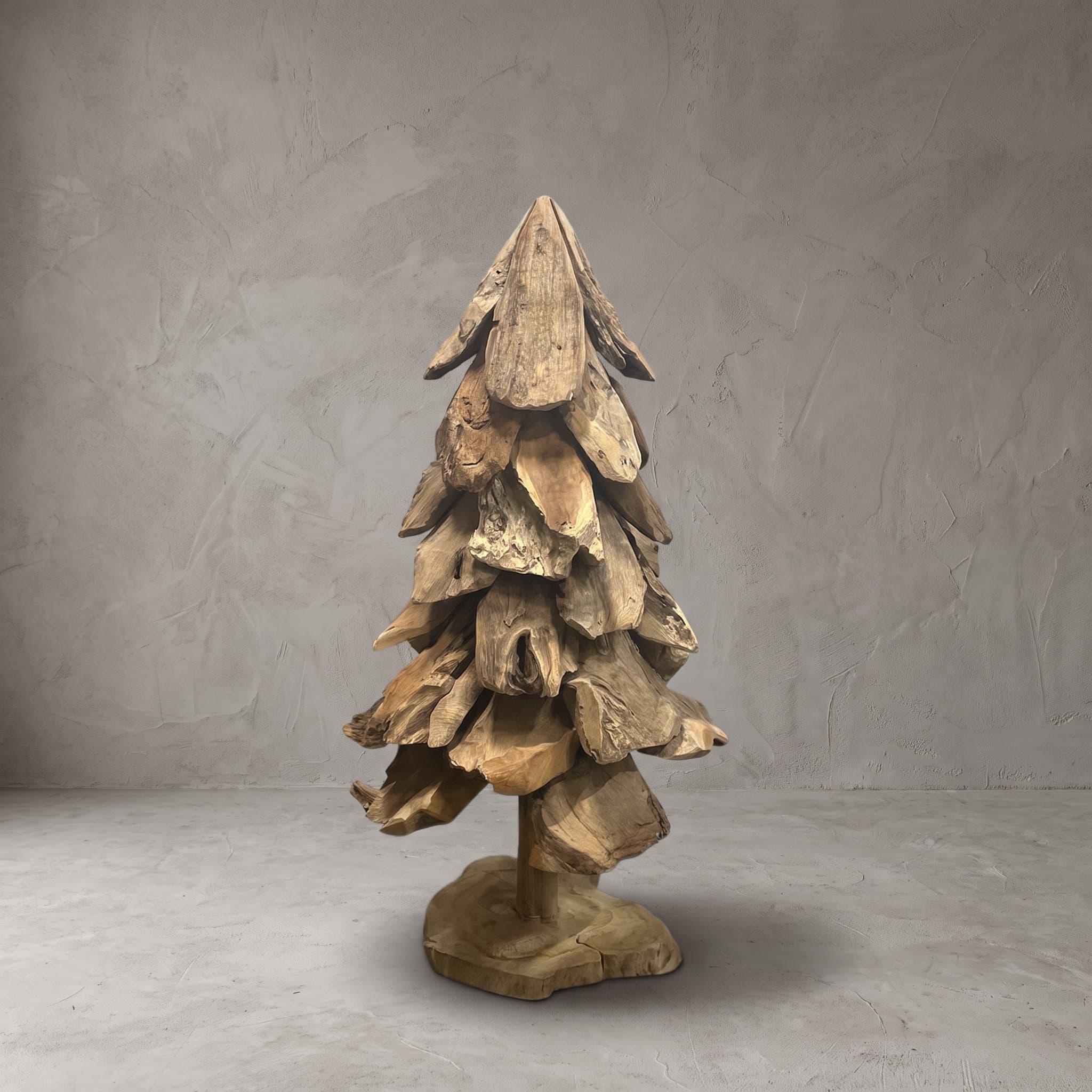 Kerstboom van gerecycled teak, vooraanzicht van de gelaagde stukken hout rond de stam op een platte voet, voor een grijze wand