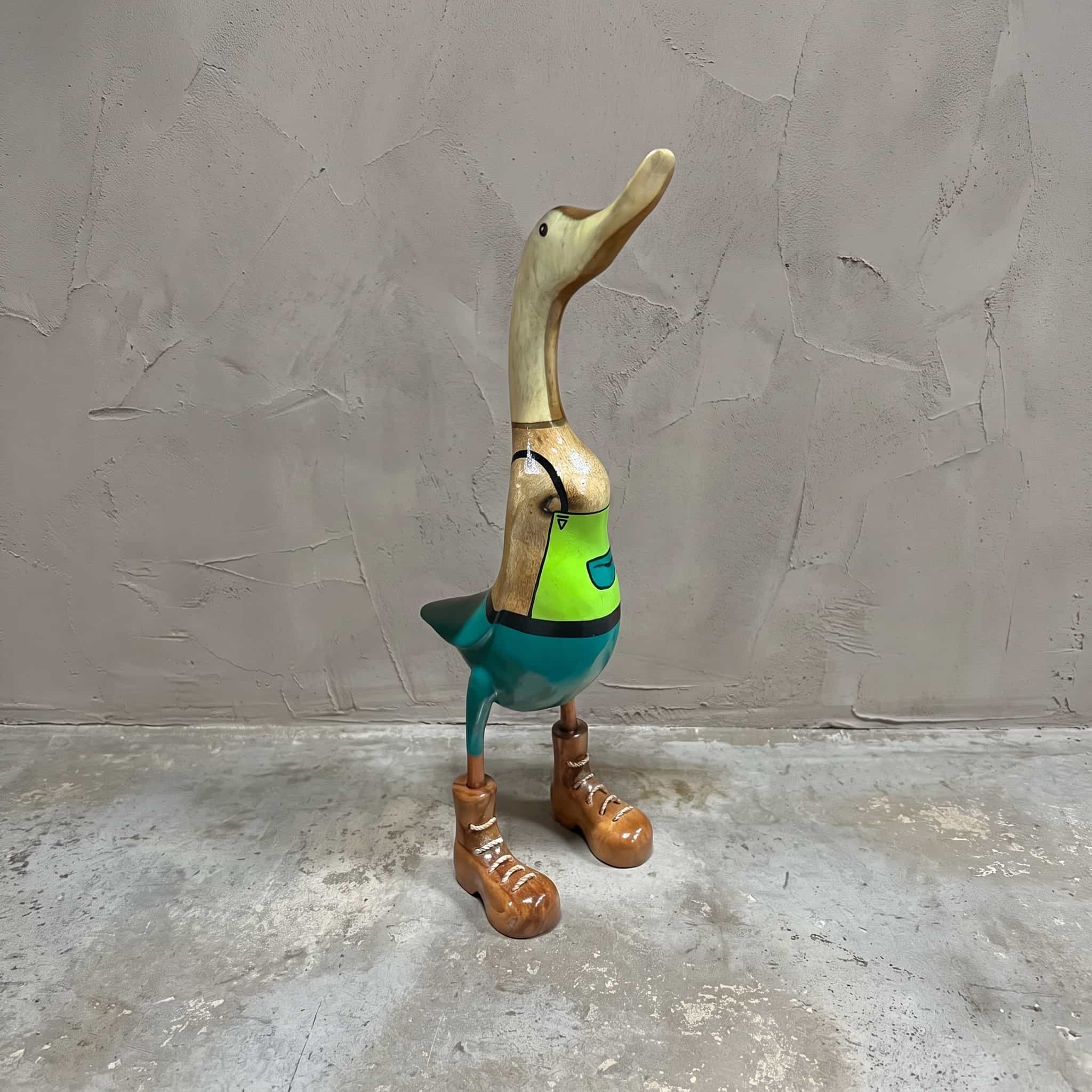 Eend van bamboe als tuinman, vooraanzicht van de eend in groene tuinbroek en bruine schoenen voor een grijze wand