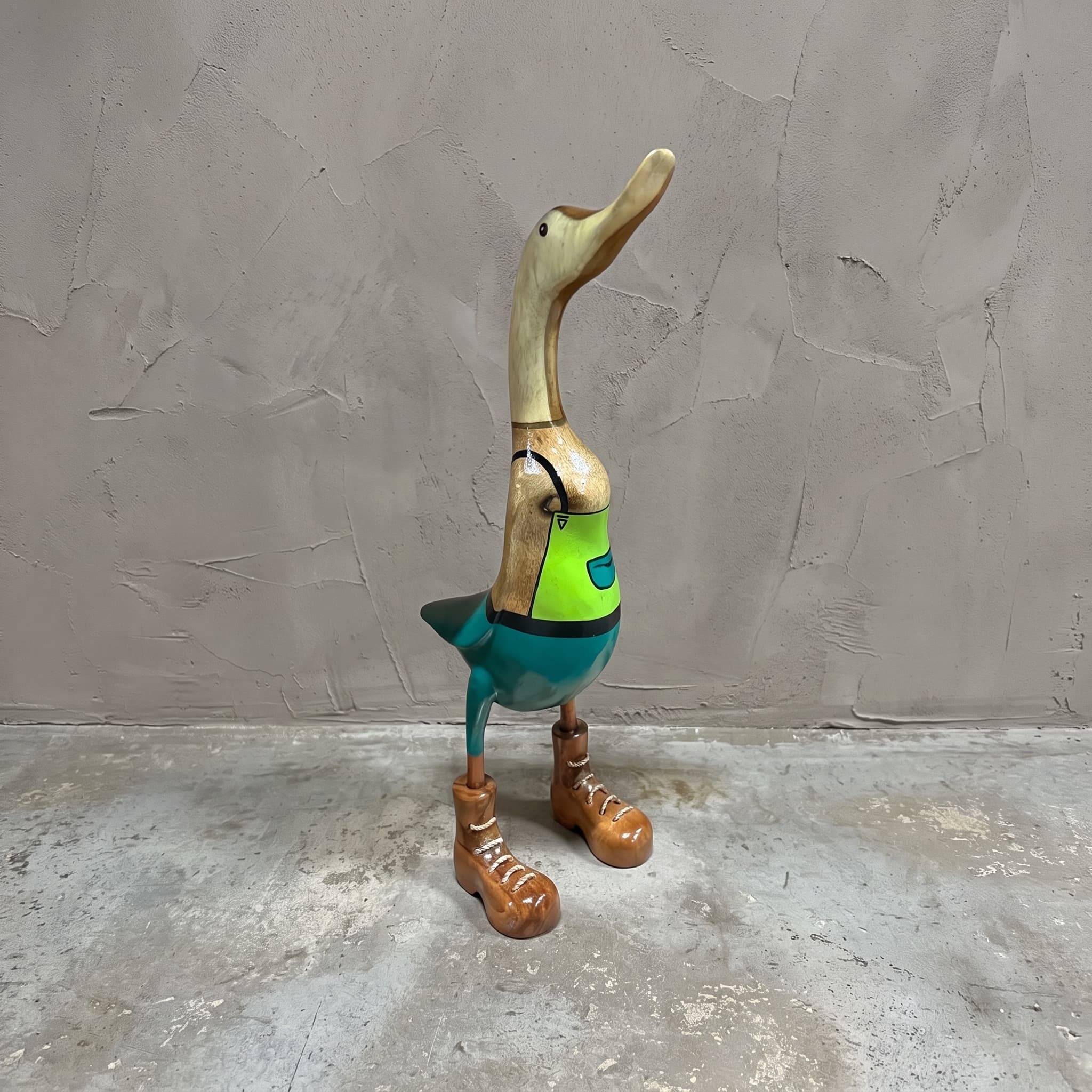 Eend van bamboe als tuinman, vooraanzicht van de eend in groene tuinbroek en bruine schoenen voor een grijze wand