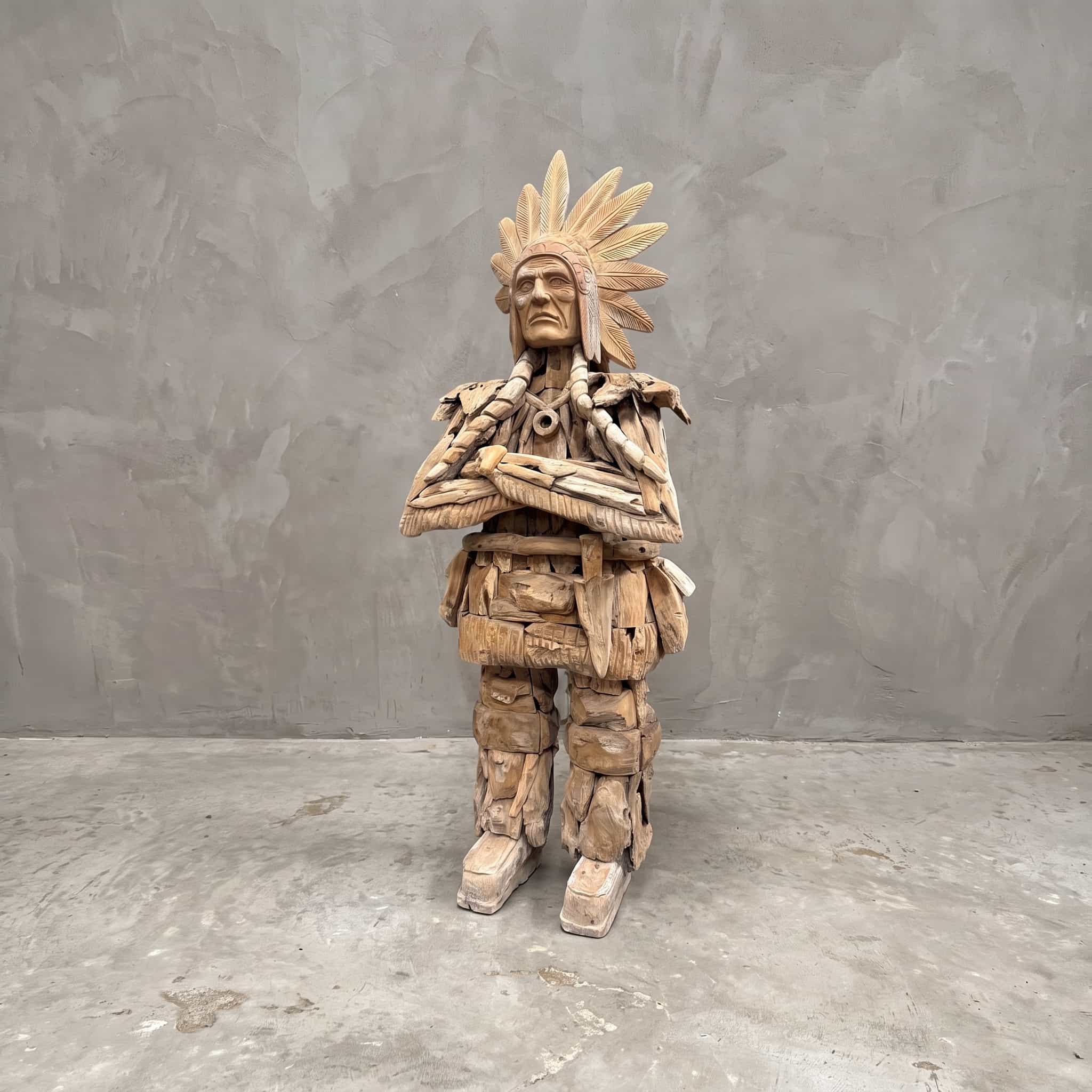 Indiaan van gerecycled teak, vooraanzicht van de staande figuur met verentooi en gekruiste armen voor een grijze wand