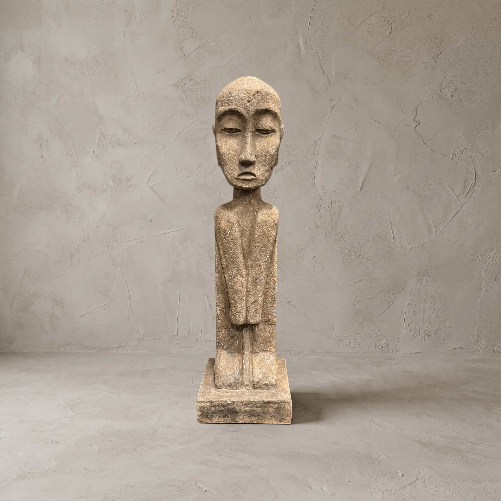 Beeld Konggo 2 van polystone, zandkleurig, vooraanzicht van de figuur met kaal hoofd en dunne hals voor een grijze wand