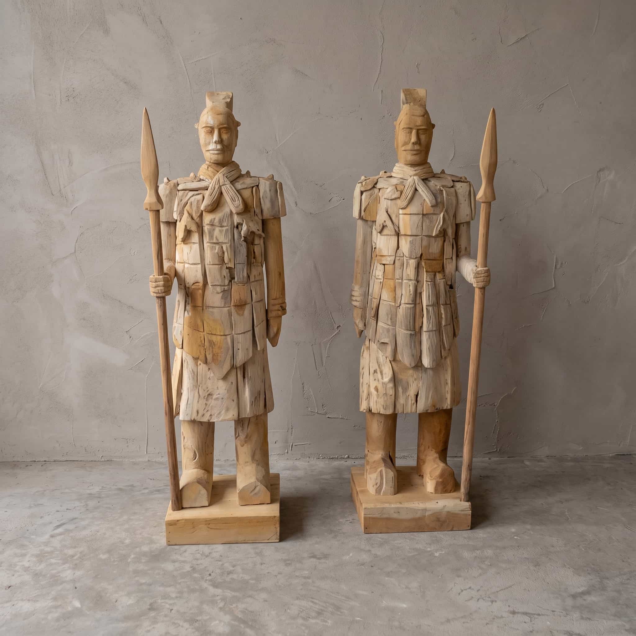 Krijger van gerecycled teak met speer, rechtshandig, twee krijgers met een speer naast elkaar, van voren gezien voor een grijze wand