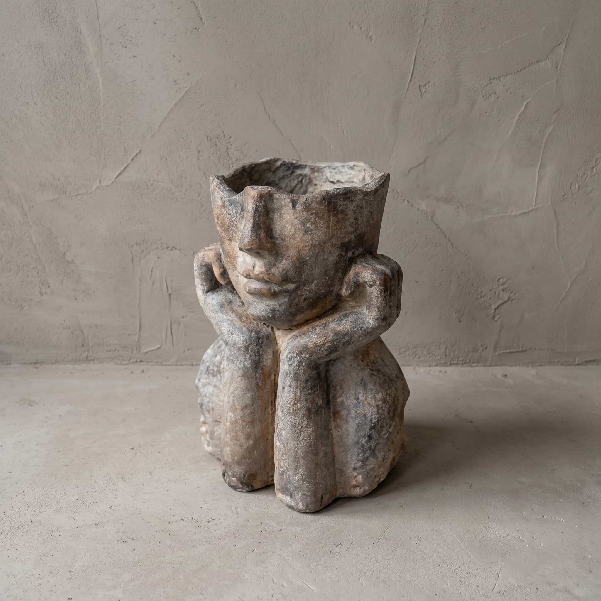 Pot van polystone, zittende figuur, vooraanzicht met het gezicht in beide handen en de opening boven de neus