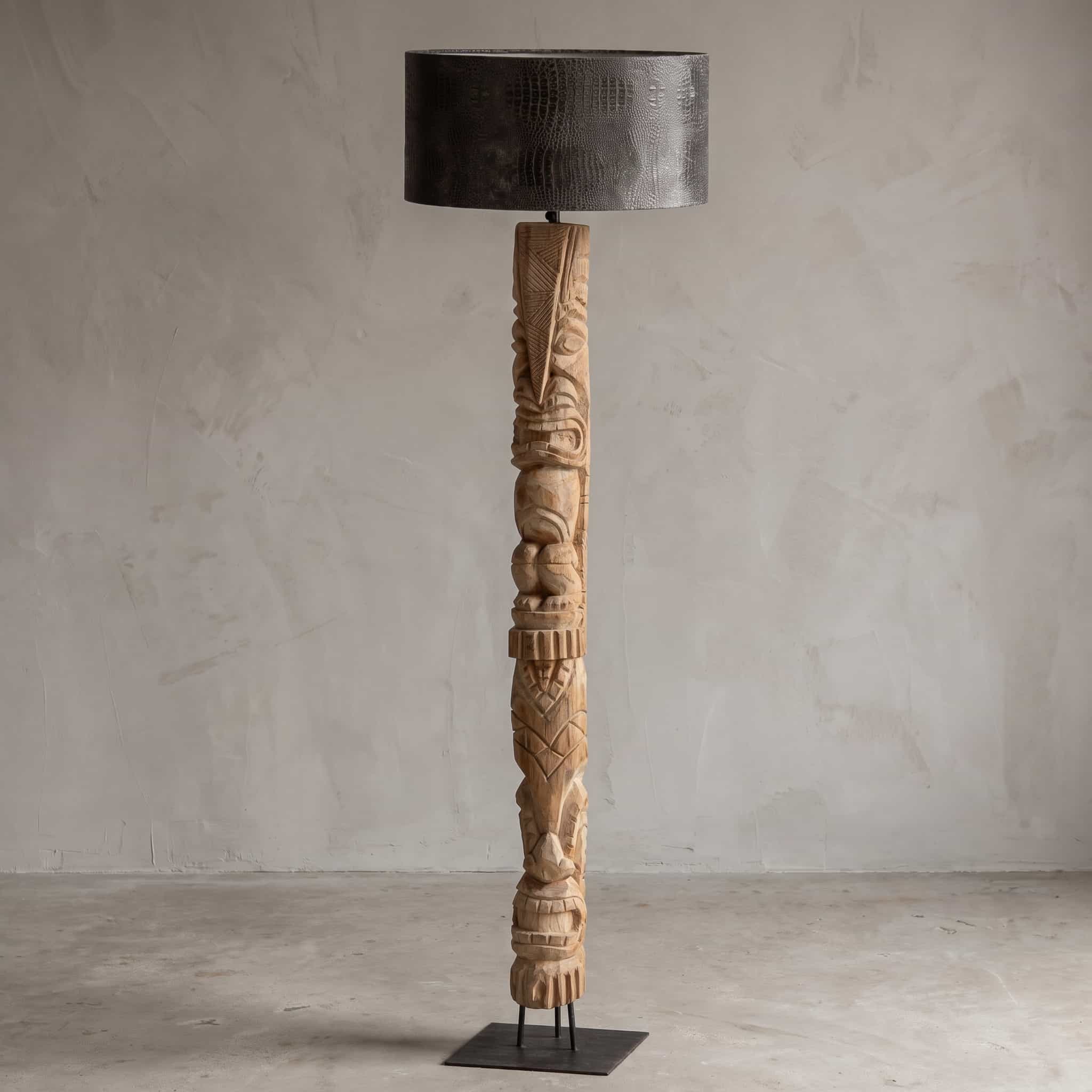 Lamp van teak en metaal, totemvorm, vooraanzicht van de lichte totem met figuren in reliëf op een vierkante voetplaat