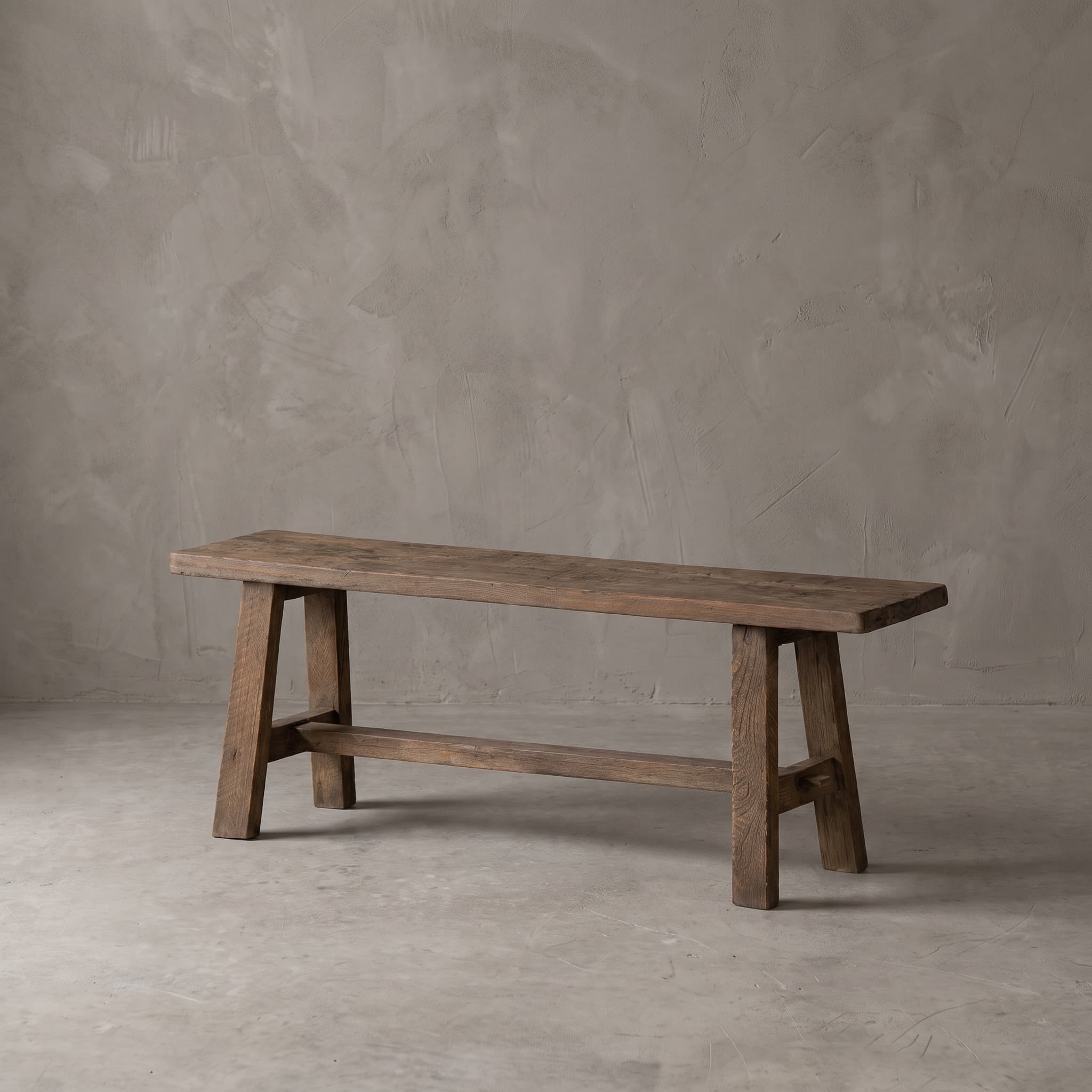 Bank School van gerecycled teak, schuin aanzicht van het gesleten blad en de lat die door de poten heen steekt