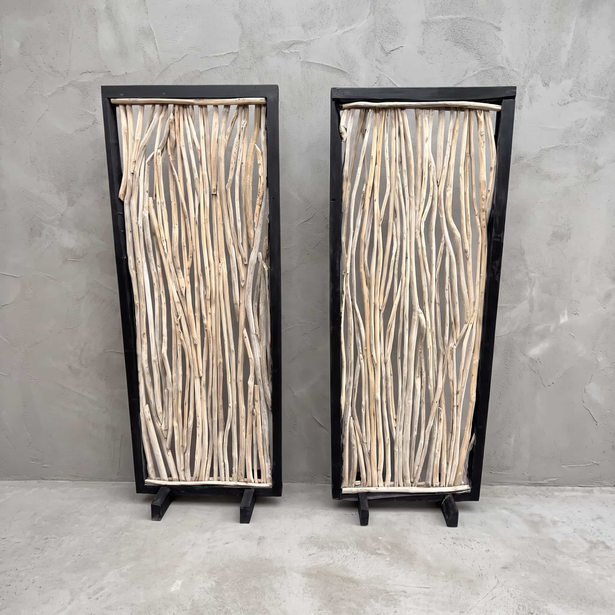 Roomdivider Ranting van teak, vooraanzicht van het zwarte frame met lichte takken, met een tweede roomdivider ernaast tegen een grijze wand