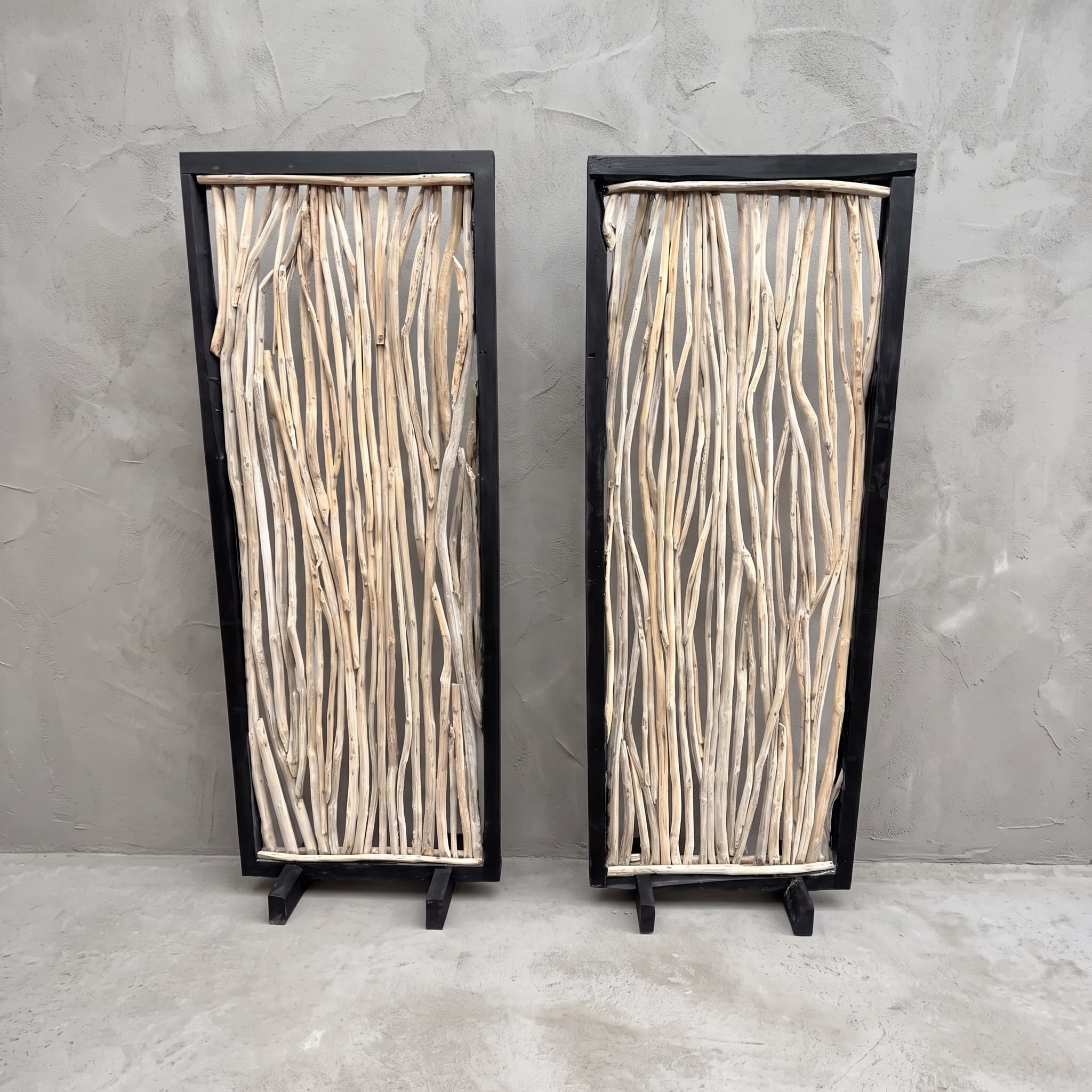 Roomdivider Ranting van teak, vooraanzicht van het zwarte frame met lichte takken, met een tweede roomdivider ernaast tegen een grijze wand