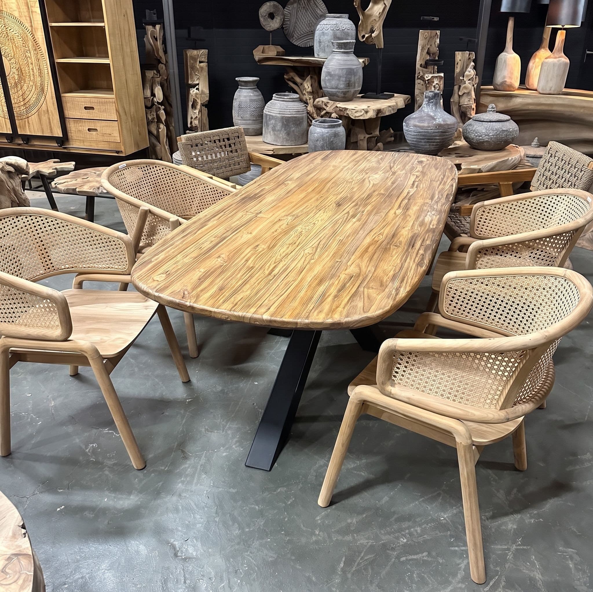 Tafelblad Donny van teak, Deens ovaal, als eettafel op een zwart onderstel met gevlochten teakhouten stoelen in de showroom