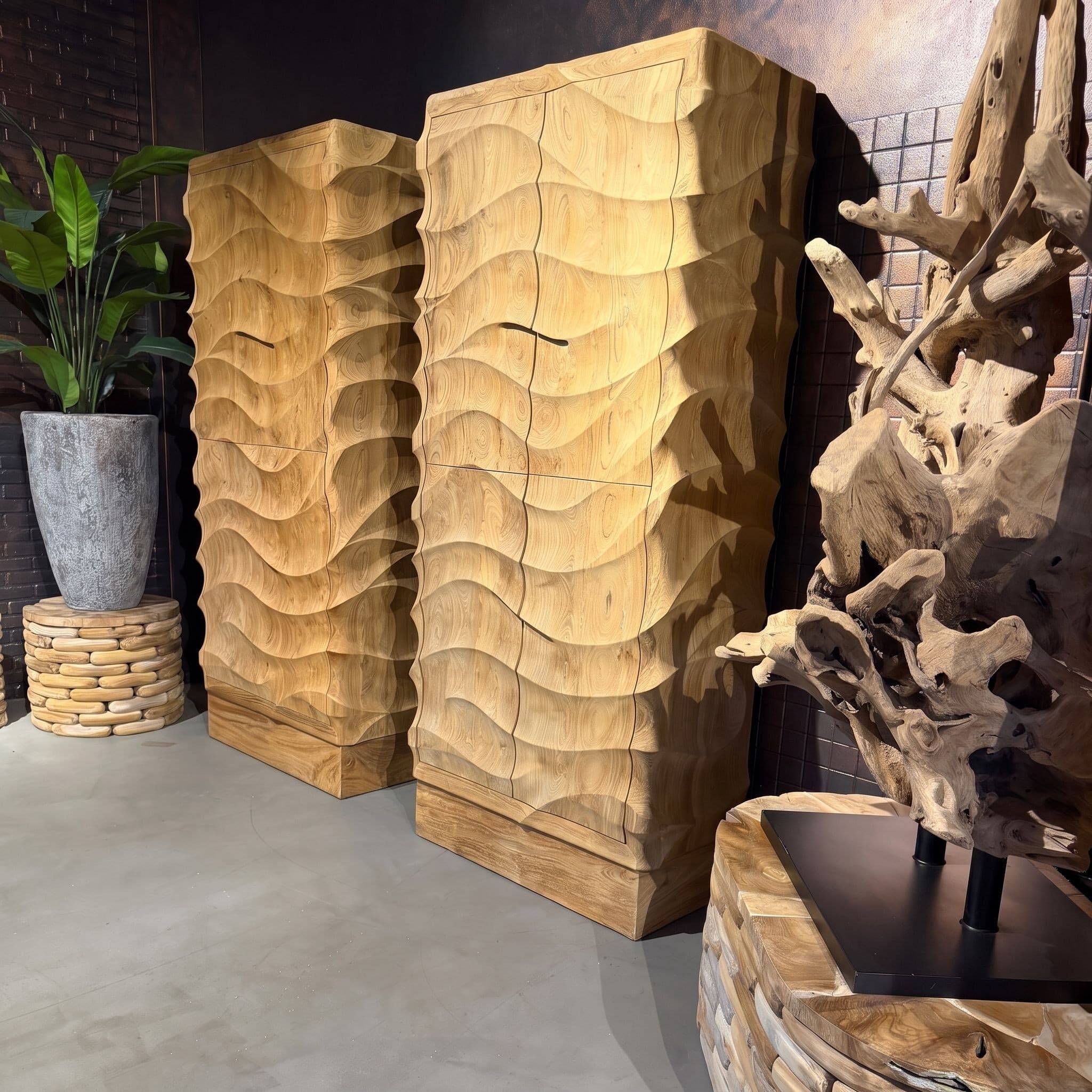 Kast Wave van teak, 210 cm hoog, twee kasten met gesneden golven naast elkaar in de showroom, bij een plant en een wortelbeeld