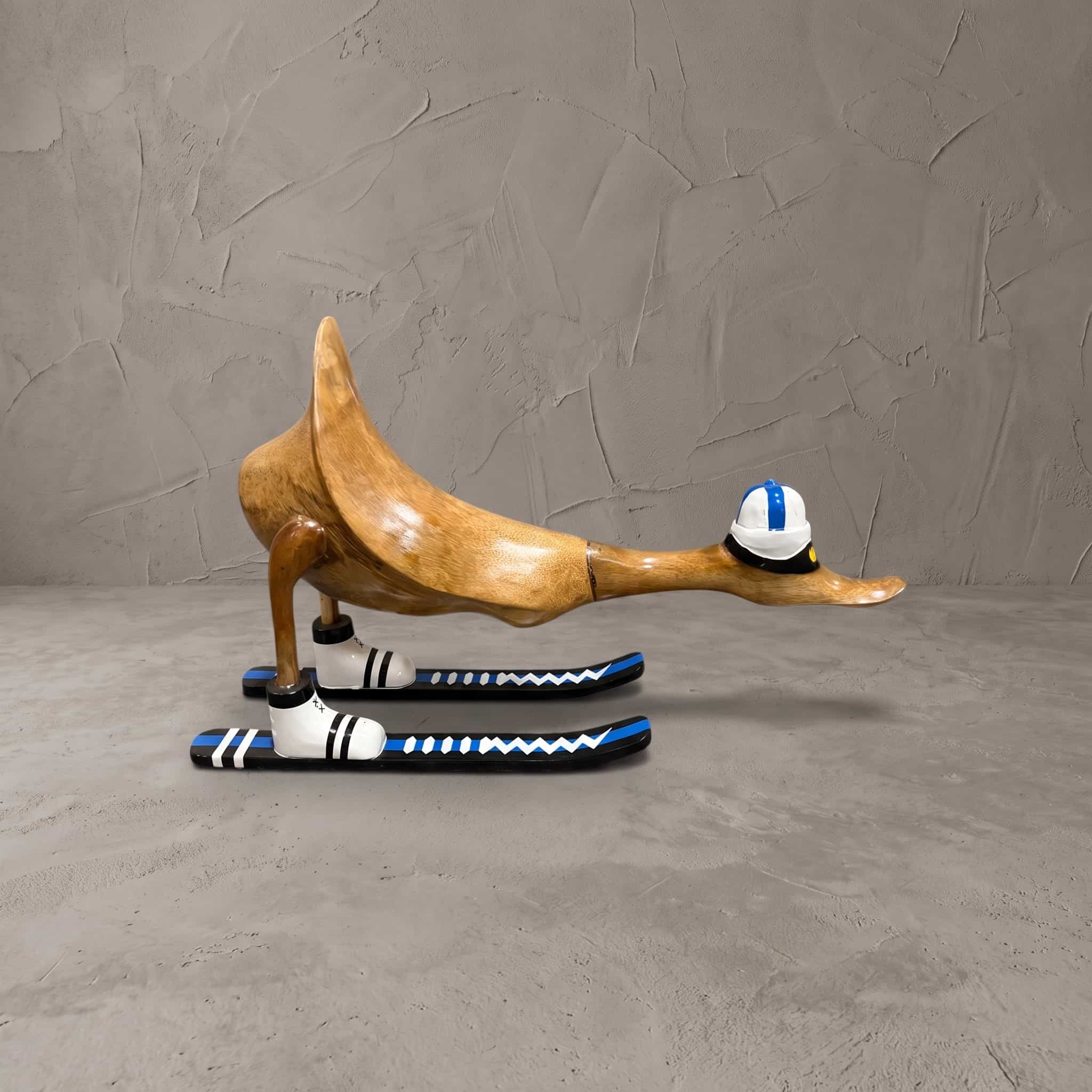 Eend van bamboe met ski's in blauw, zijaanzicht van de voorovergebogen eend met helm voor een grijze wand