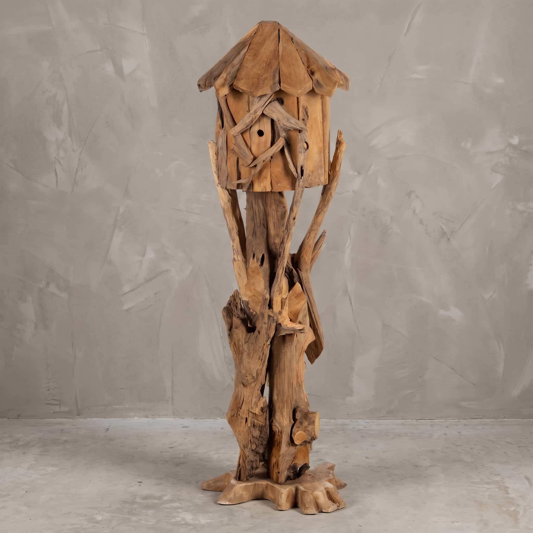 Standaard van teak, gesloten vogelhuisje, vooraanzicht van het huisje tussen takken op een grillige stam voor een grijze wand