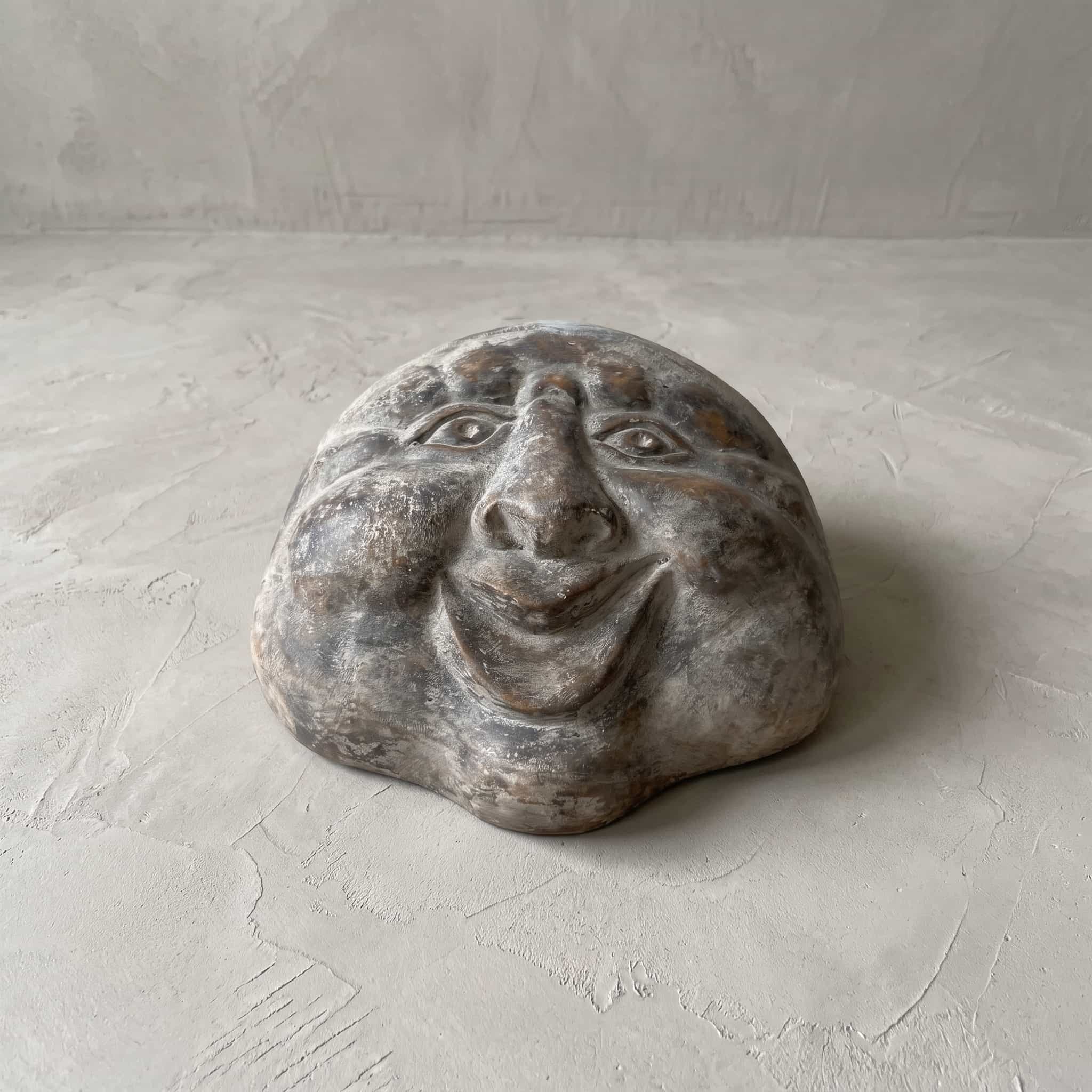Beeld Moon Senyum van polystone, vooraanzicht van het lachende gezicht dat plat op een betonvloer ligt