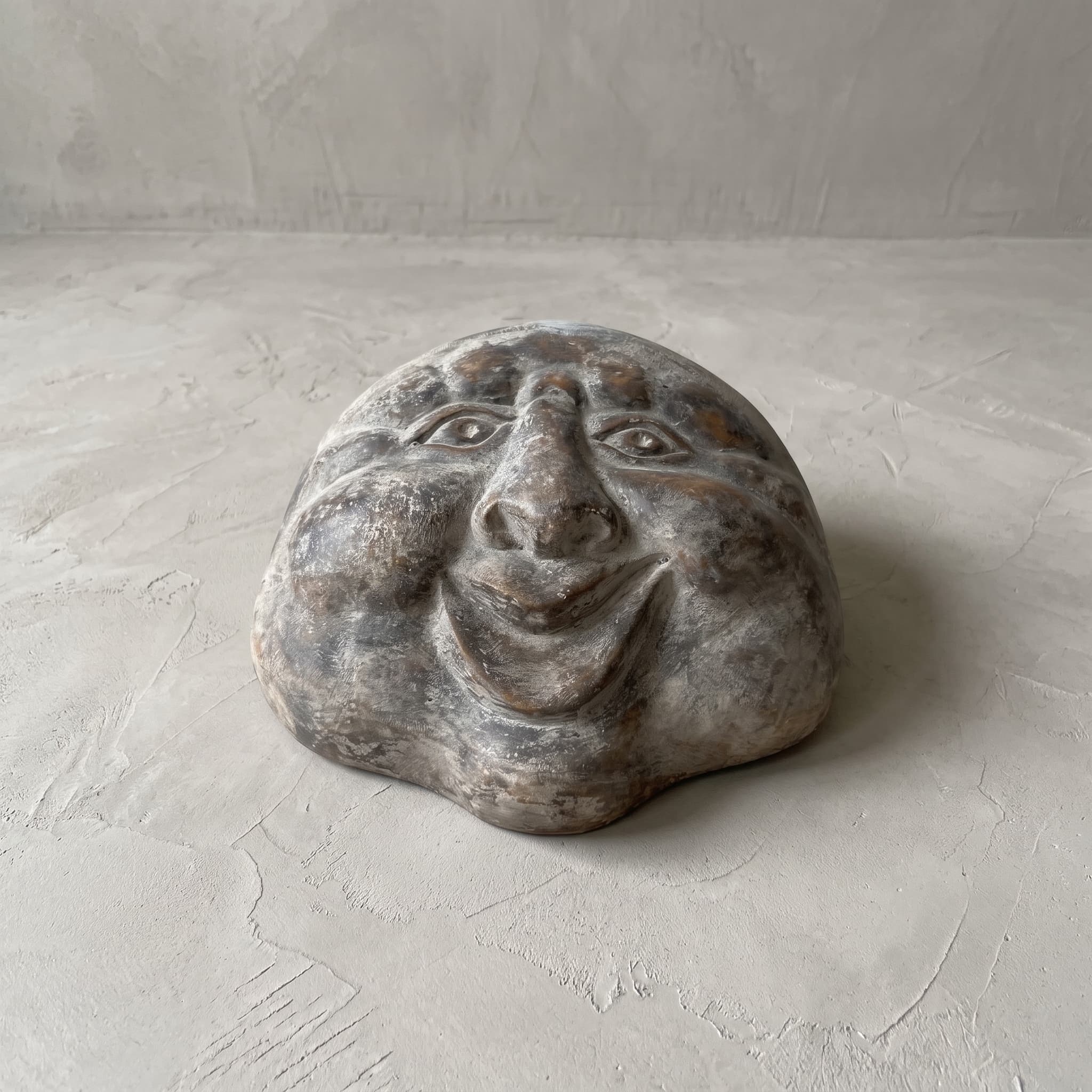 Beeld Moon Senyum van polystone, vooraanzicht van het lachende gezicht dat plat op een betonvloer ligt