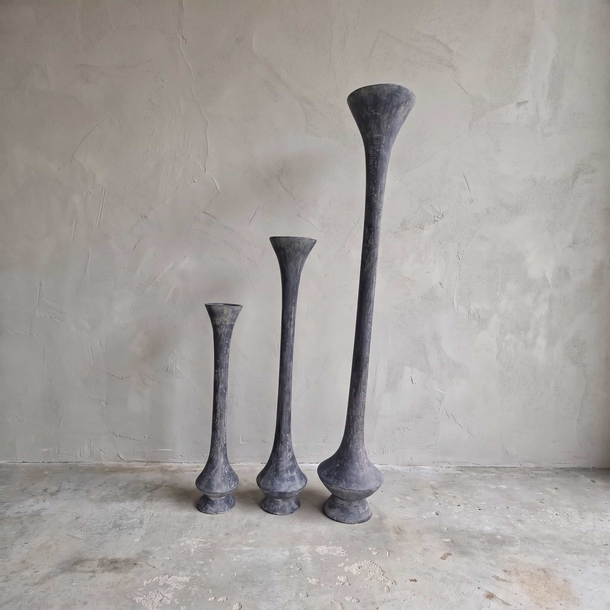 Pot van polystone, trompetvorm, 70 cm hoog, met andere maten uit de serie ernaast tegen een grijze wand