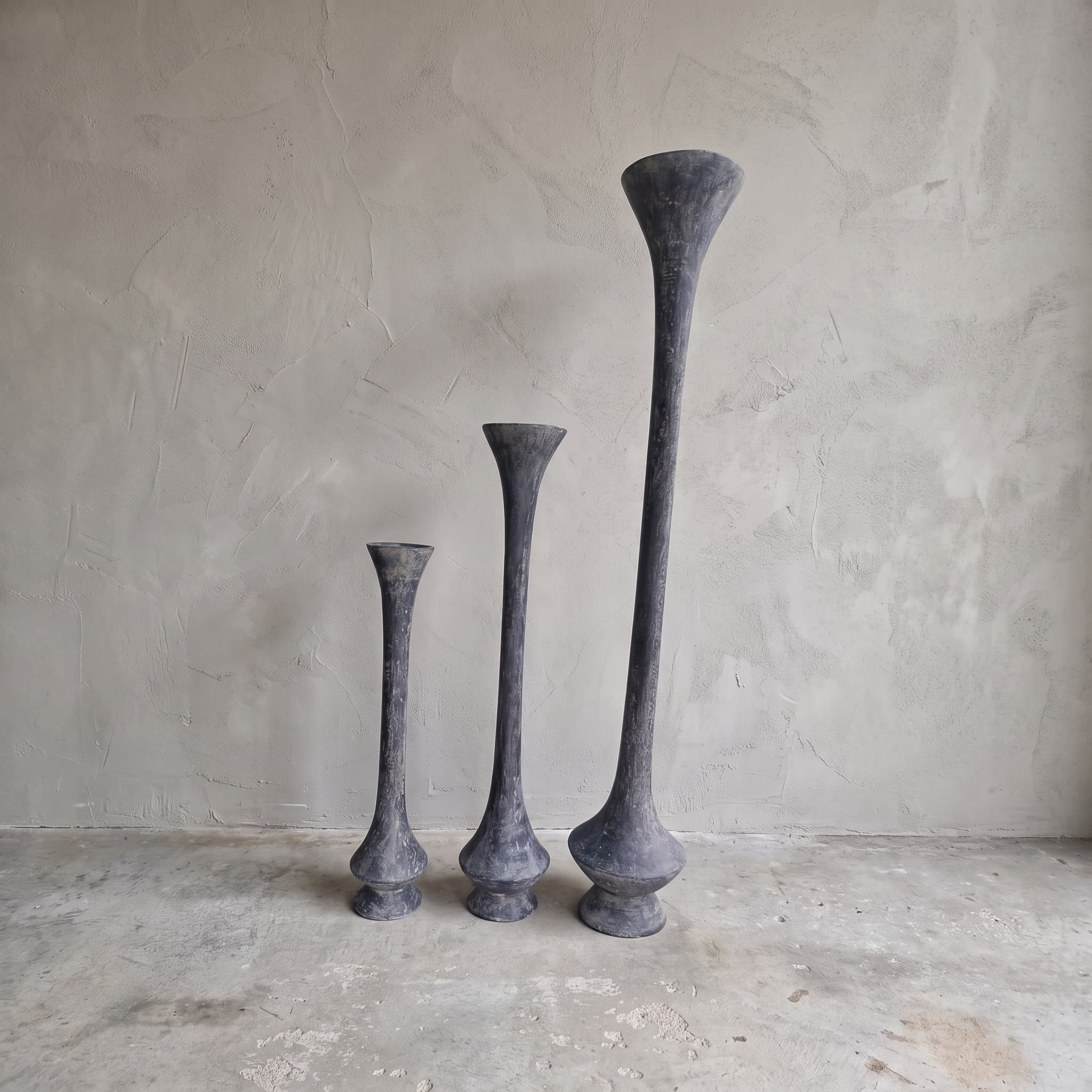 Pot van polystone, trompetvorm, 70 cm hoog, met andere maten uit de serie ernaast tegen een grijze wand