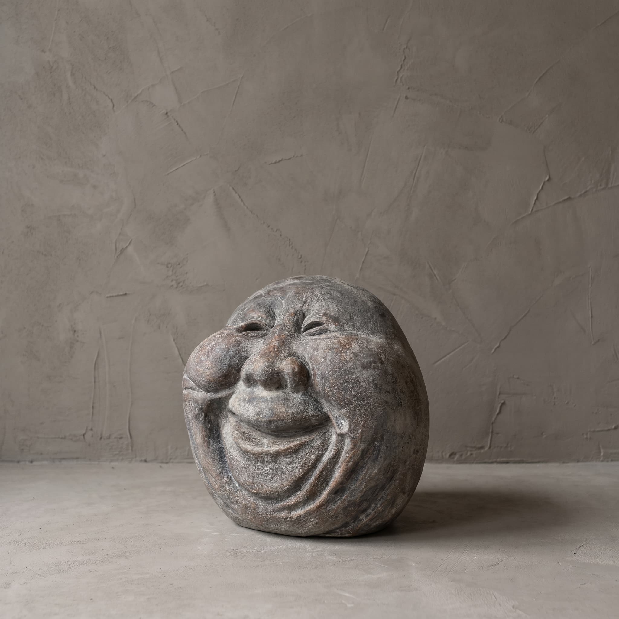 Beeld Moon Kepala van polystone, oude man, van verder weg gezien op een betonvloer voor een grijze wand