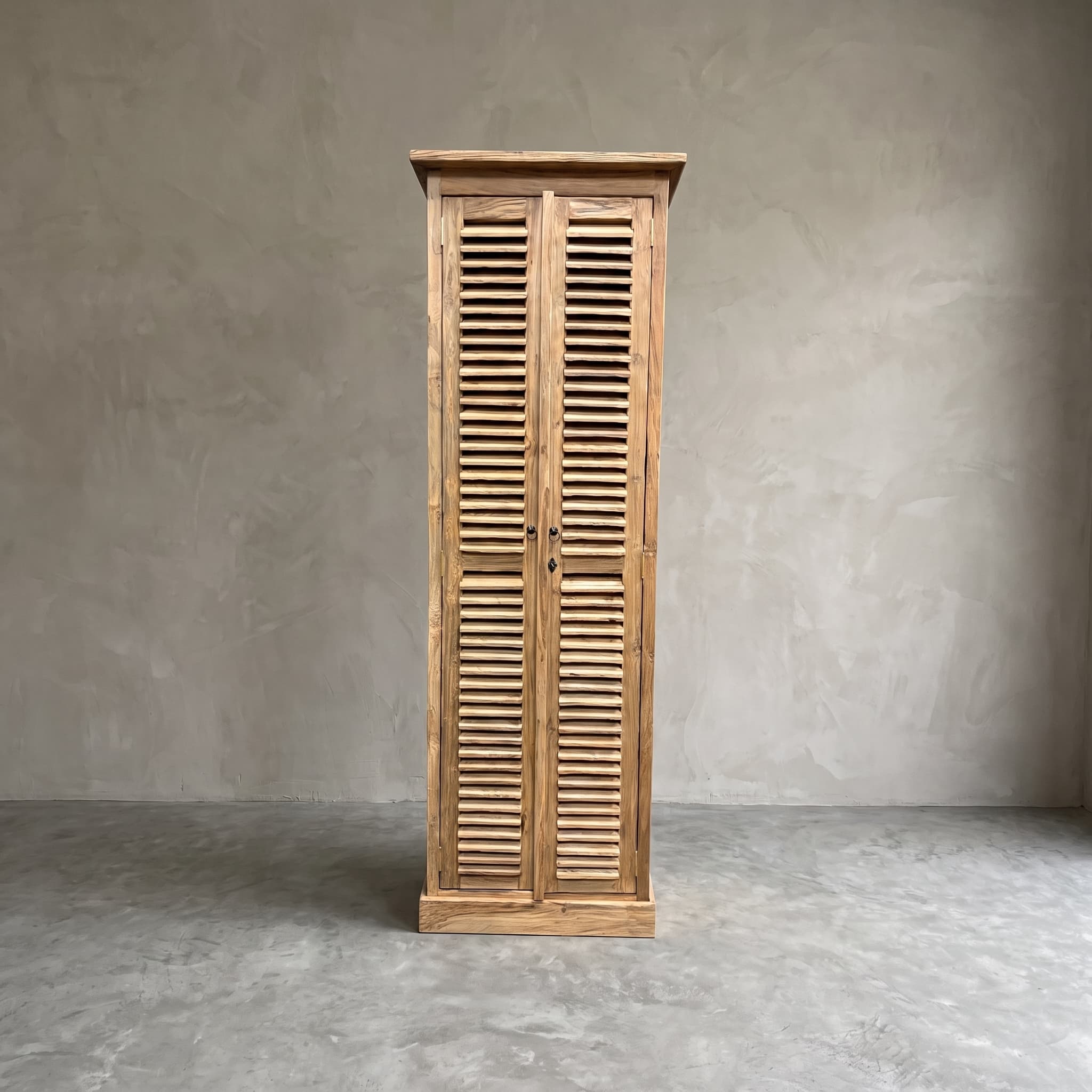 Kast Bali van gerecycled teak, 220 cm hoog, recht van voren in een lege ruimte met grijze wand en betonvloer