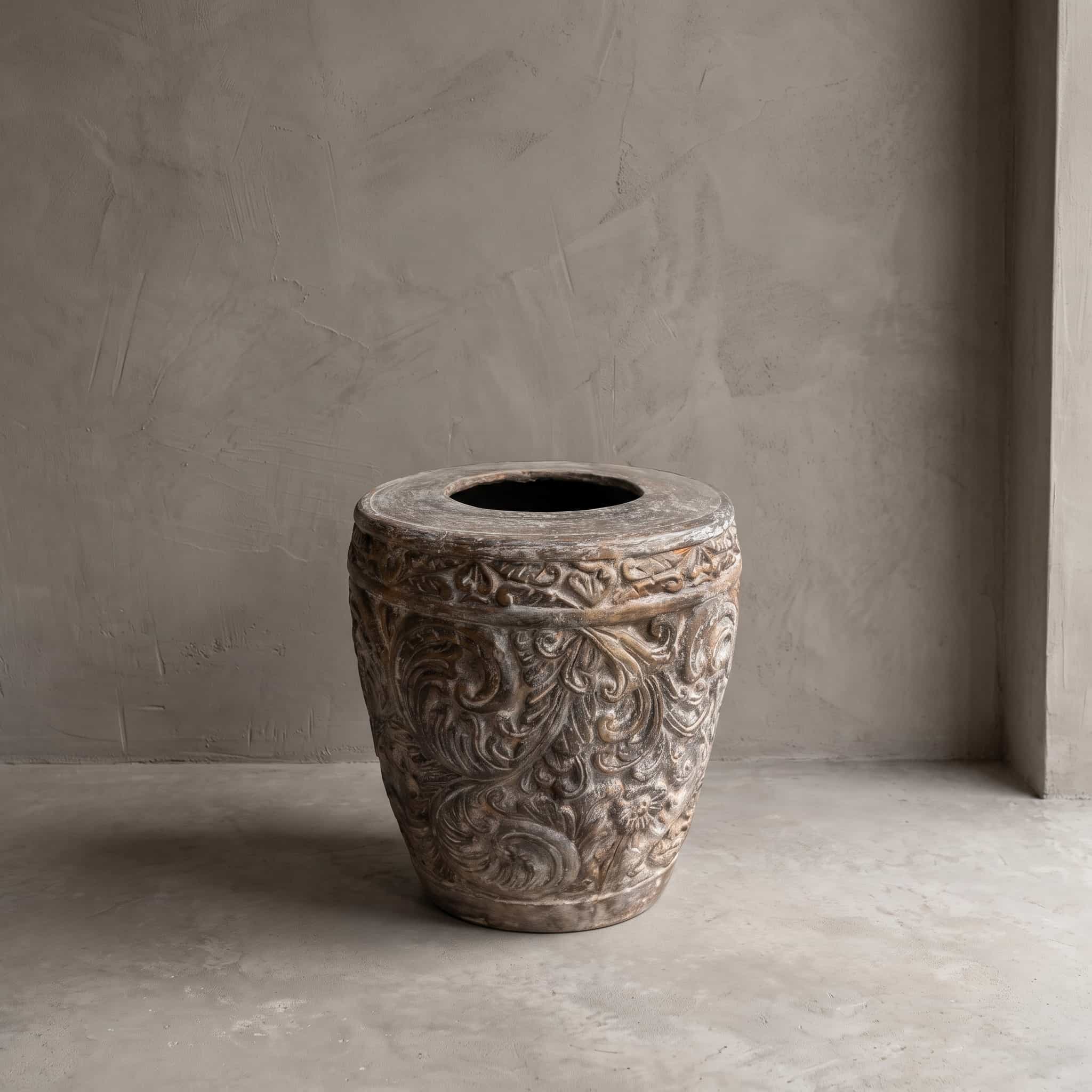 Pot Ukir van polystone in maat 60 cm, vooraanzicht met een reliëf van krullende ranken en een platte rand, op een betonvloer