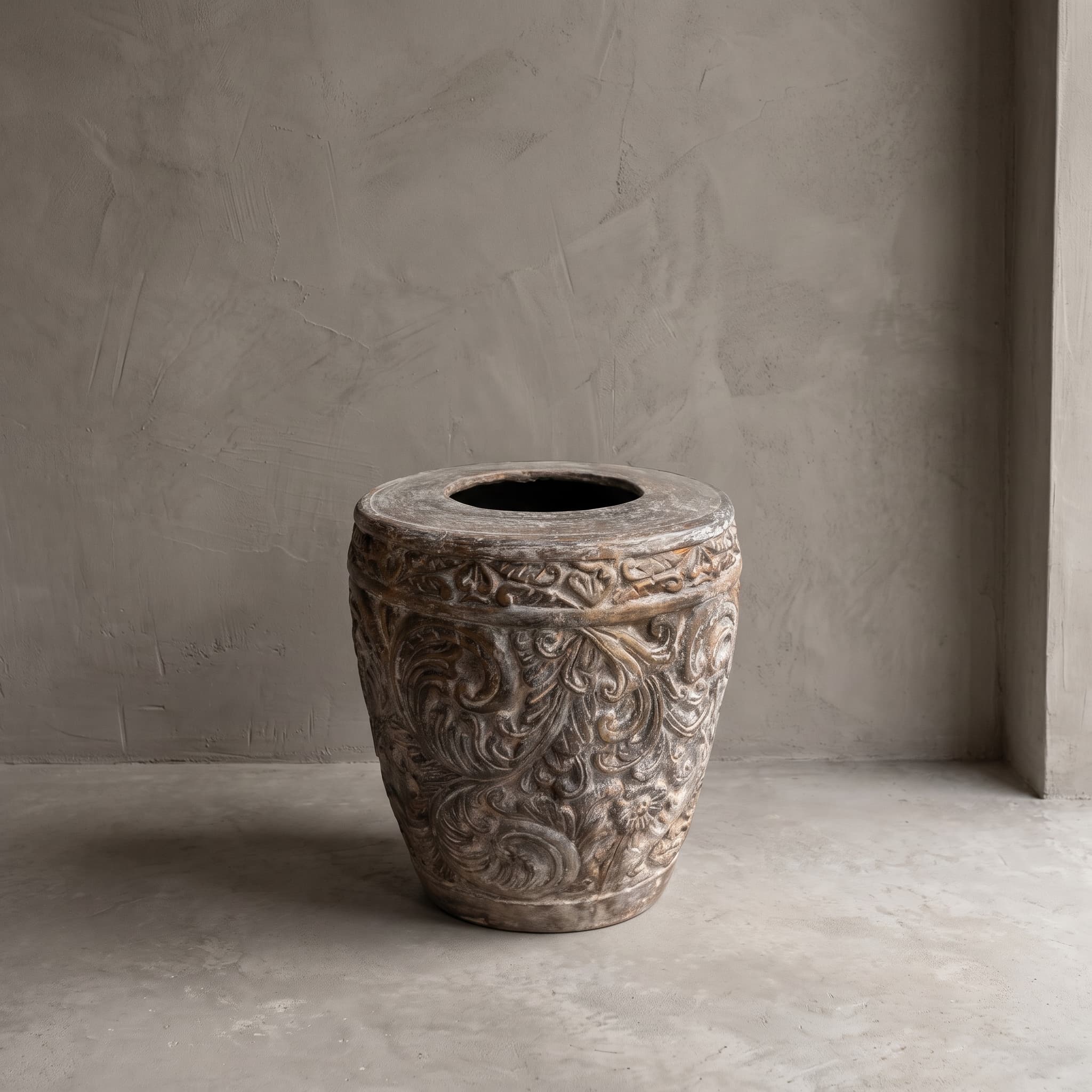 Pot Ukir van polystone in maat 60 cm, vooraanzicht met een reliëf van krullende ranken en een platte rand, op een betonvloer