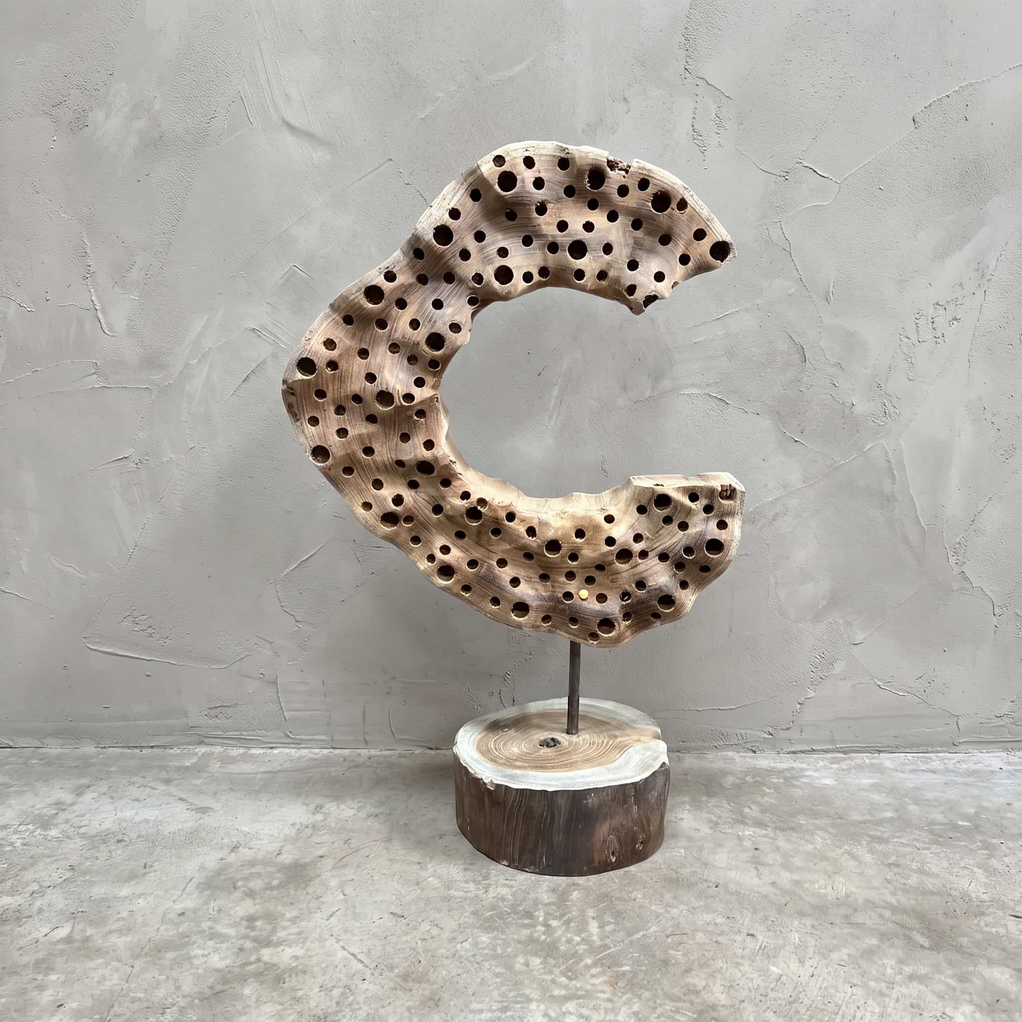 Sokkel Klirong Moon van gerecycled teak, vooraanzicht van de halvemaan met ronde gaten op de boomschijf, voor een grijze wand