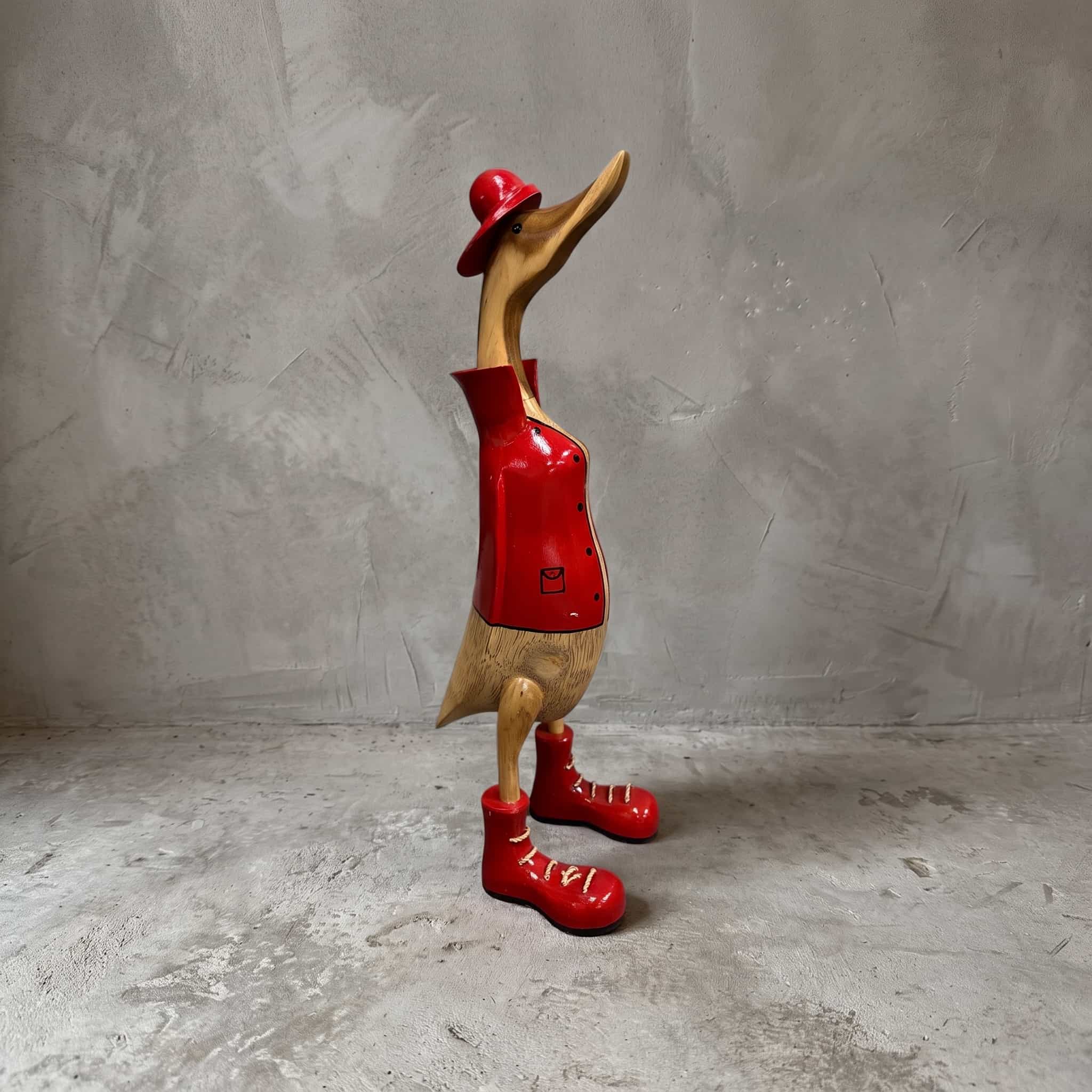 Eend van bamboe, brandweerman, van opzij in rode jas, rood hoedje en rode veterschoenen voor een grijze wand
