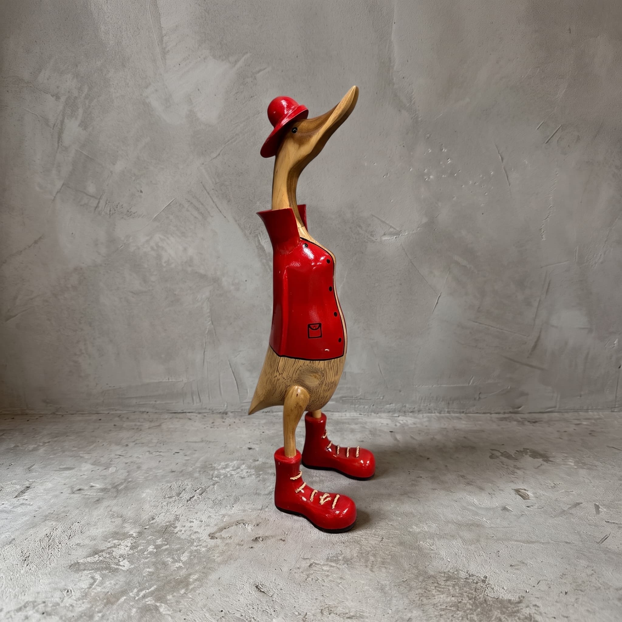 Eend van bamboe, brandweerman, van opzij in rode jas, rood hoedje en rode veterschoenen voor een grijze wand