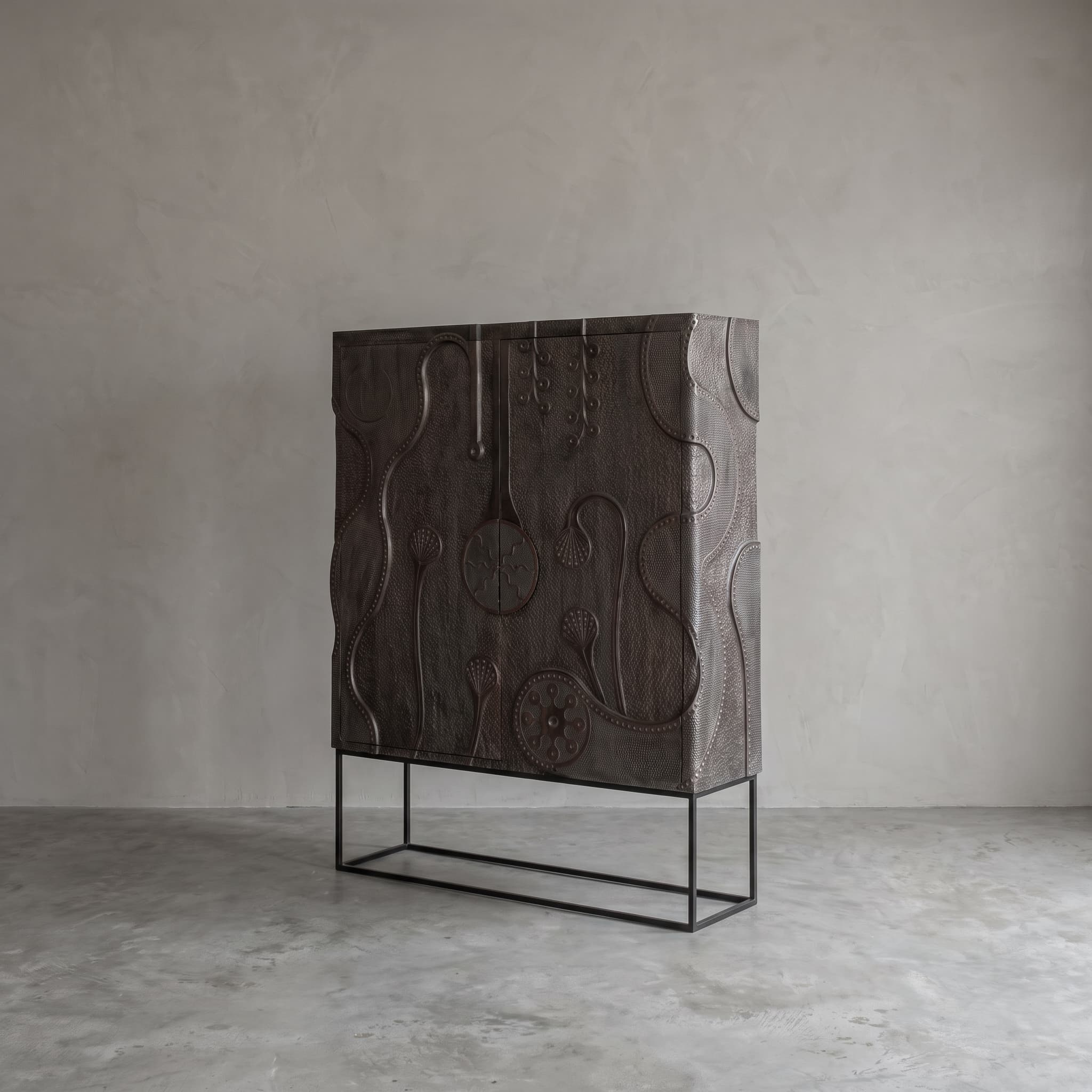 Ukiran teak cabinet seen at an angle from the front: a dark cabinet with relief on front and side, on an open base