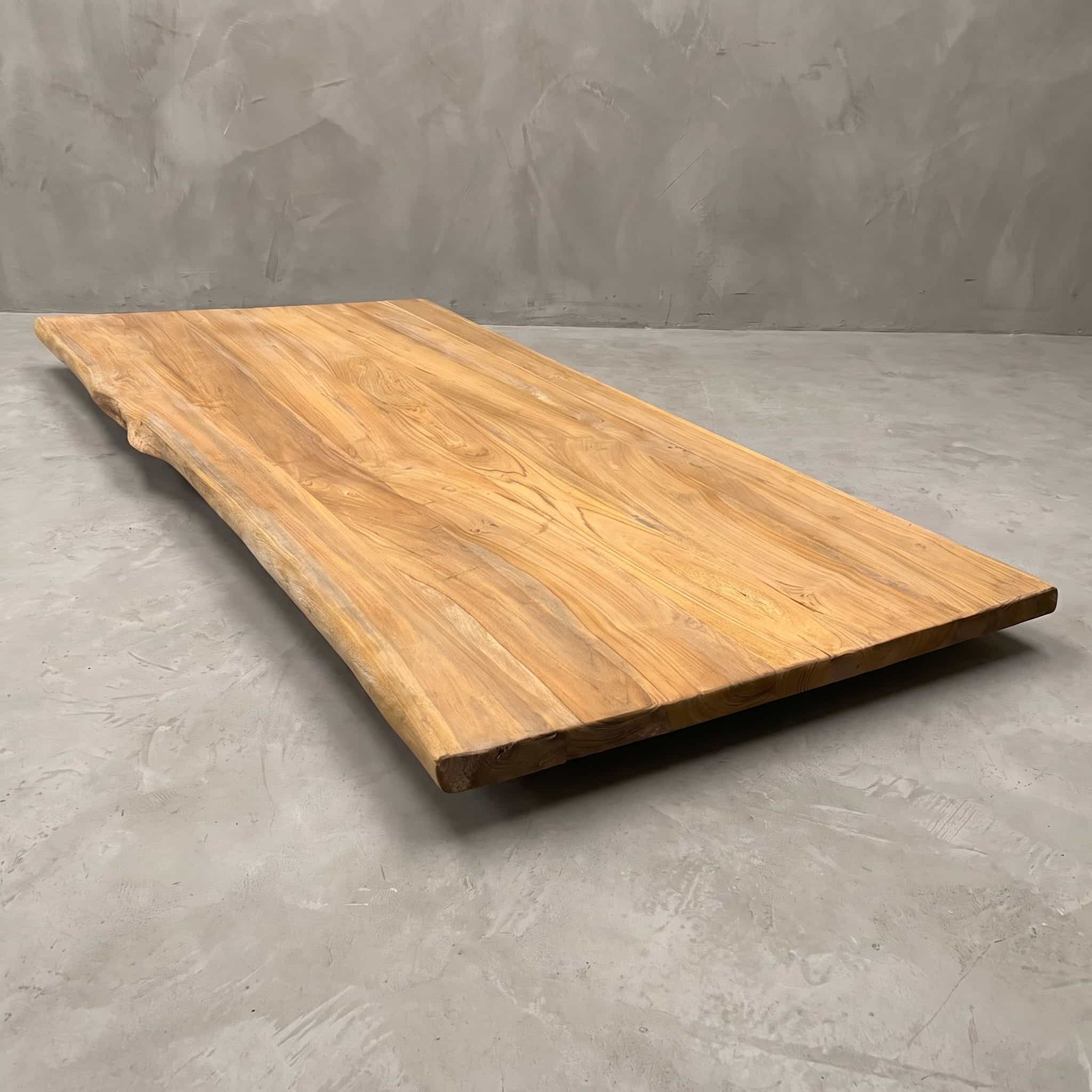 Tafelblad Kulitan van gerecycled teak, brede planken, schuin vooraanzicht met één onregelmatige lange zijde, op een betonvloer
